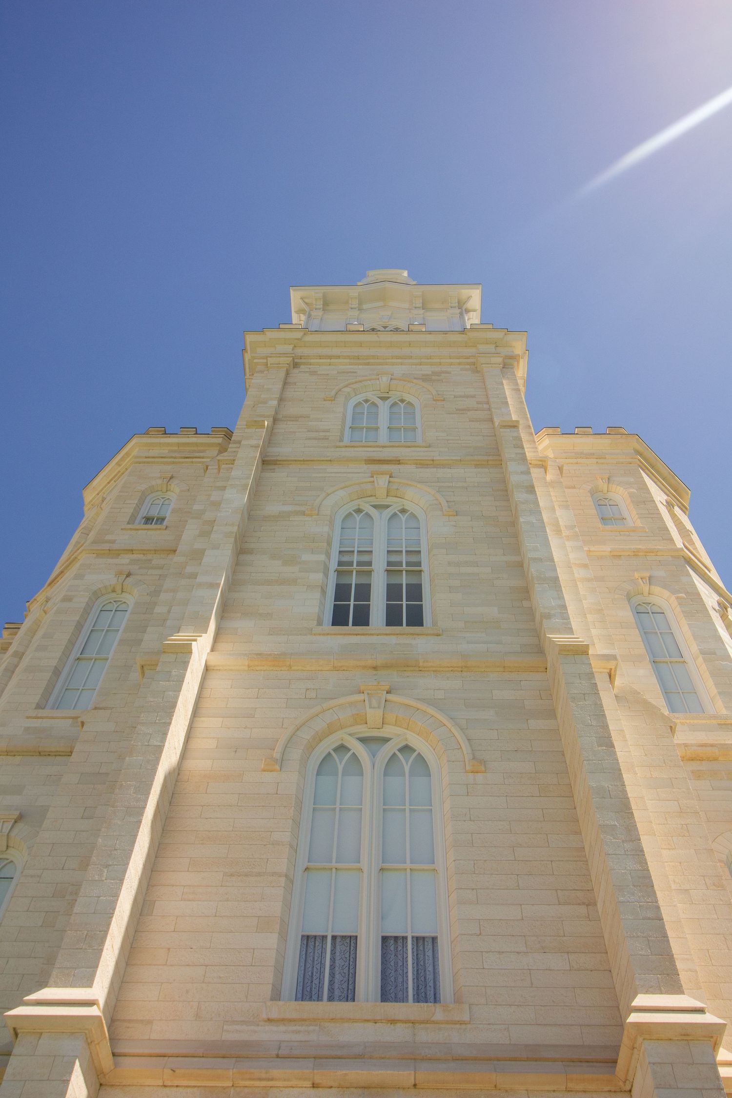 Low-angle view of a tall limestone temple tower with arched Gothic windows and ornate stonework against a clear blue sky.