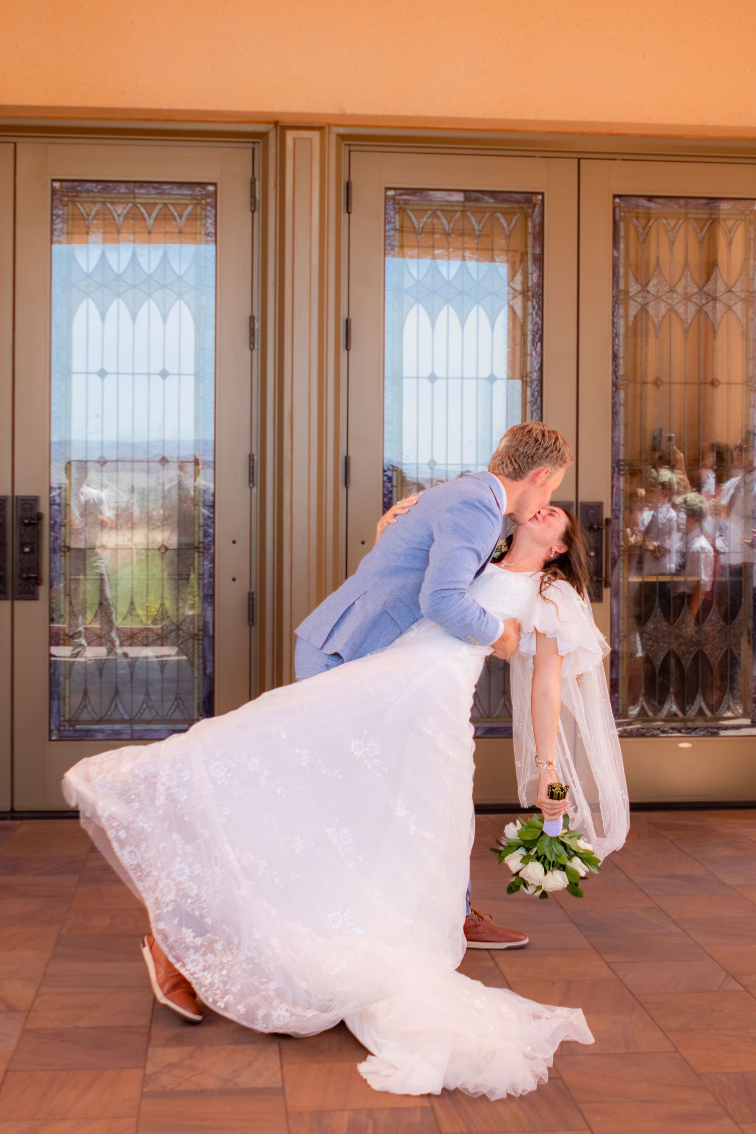 Groom in blue suit dips bride in white wedding gown for a romantic kiss outside LDS Temple Doors in Southern Utah. Church of Jesus Christ