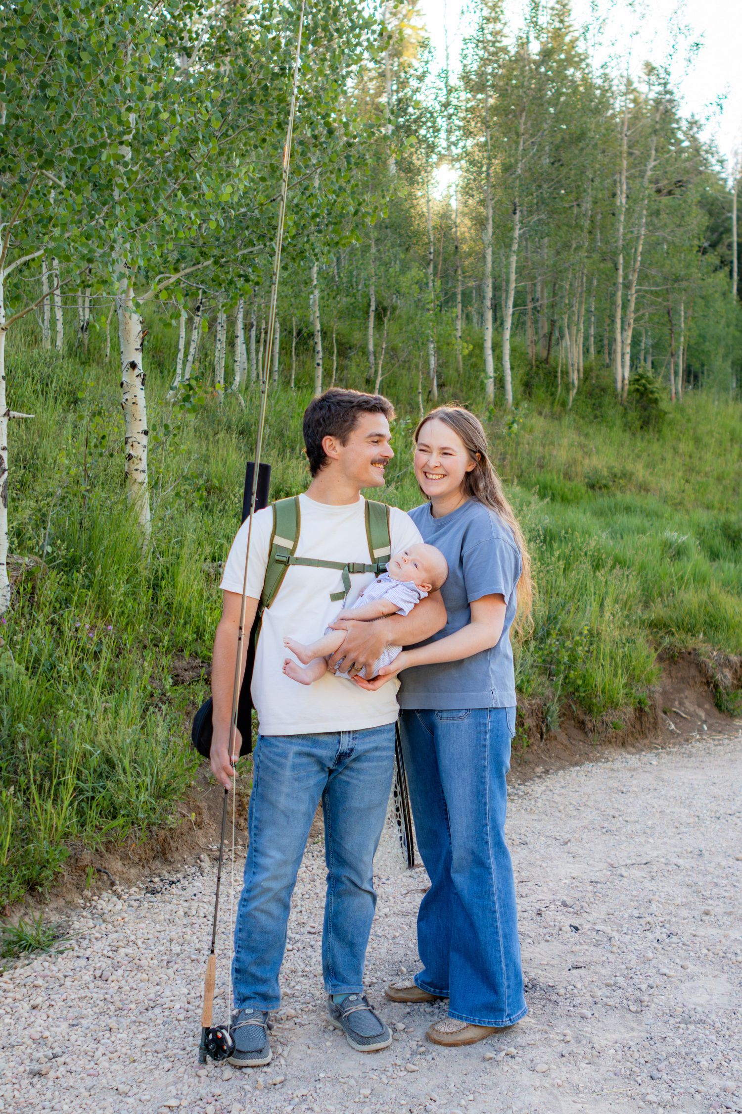Young couple with baby hiking on a forest trail surrounded by aspen trees on a sunny day.