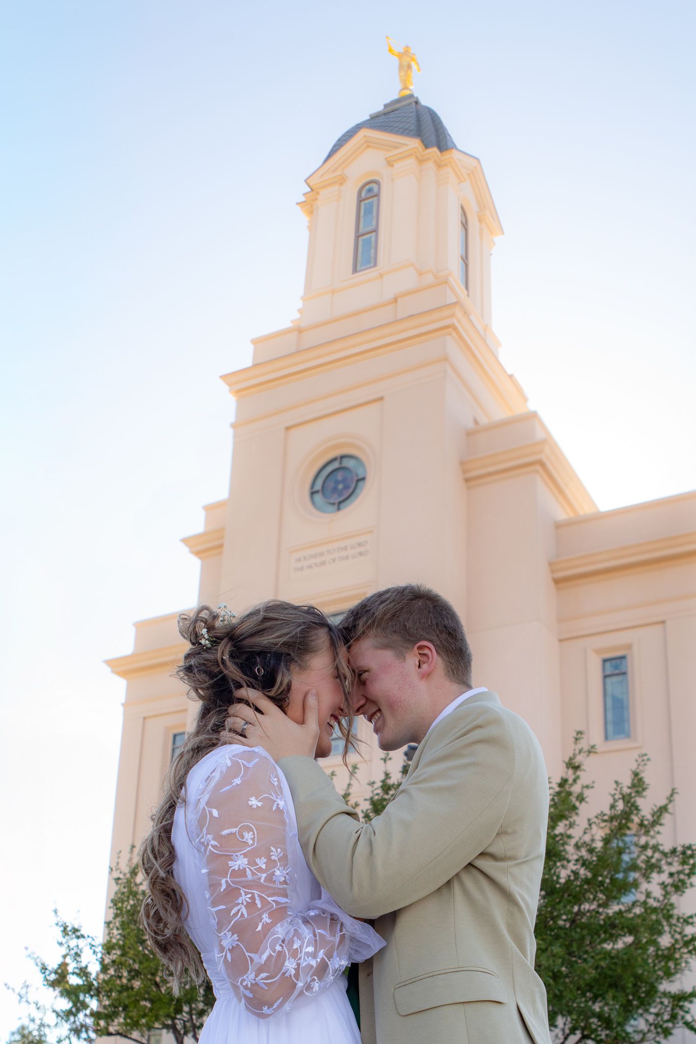 Bride and groom share a romantic moment outside an LDS temple with a golden angel Moroni statue on the steeple.