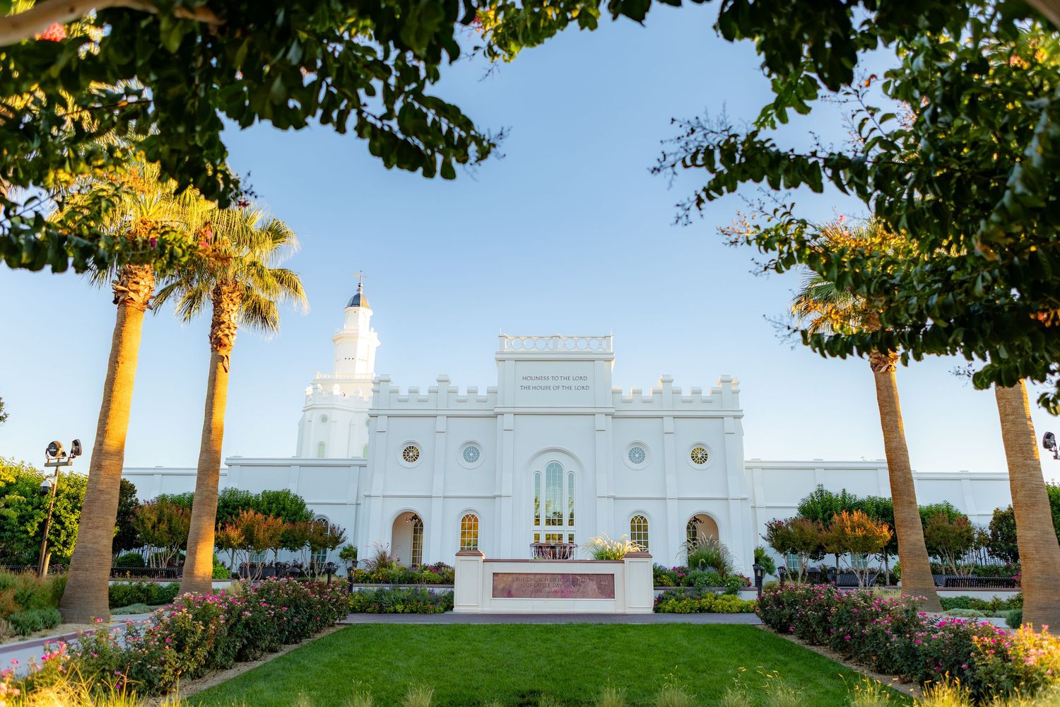 White LDS temple with ornate architecture surrounded by lush palm trees and manicured gardens under a clear blue sky.