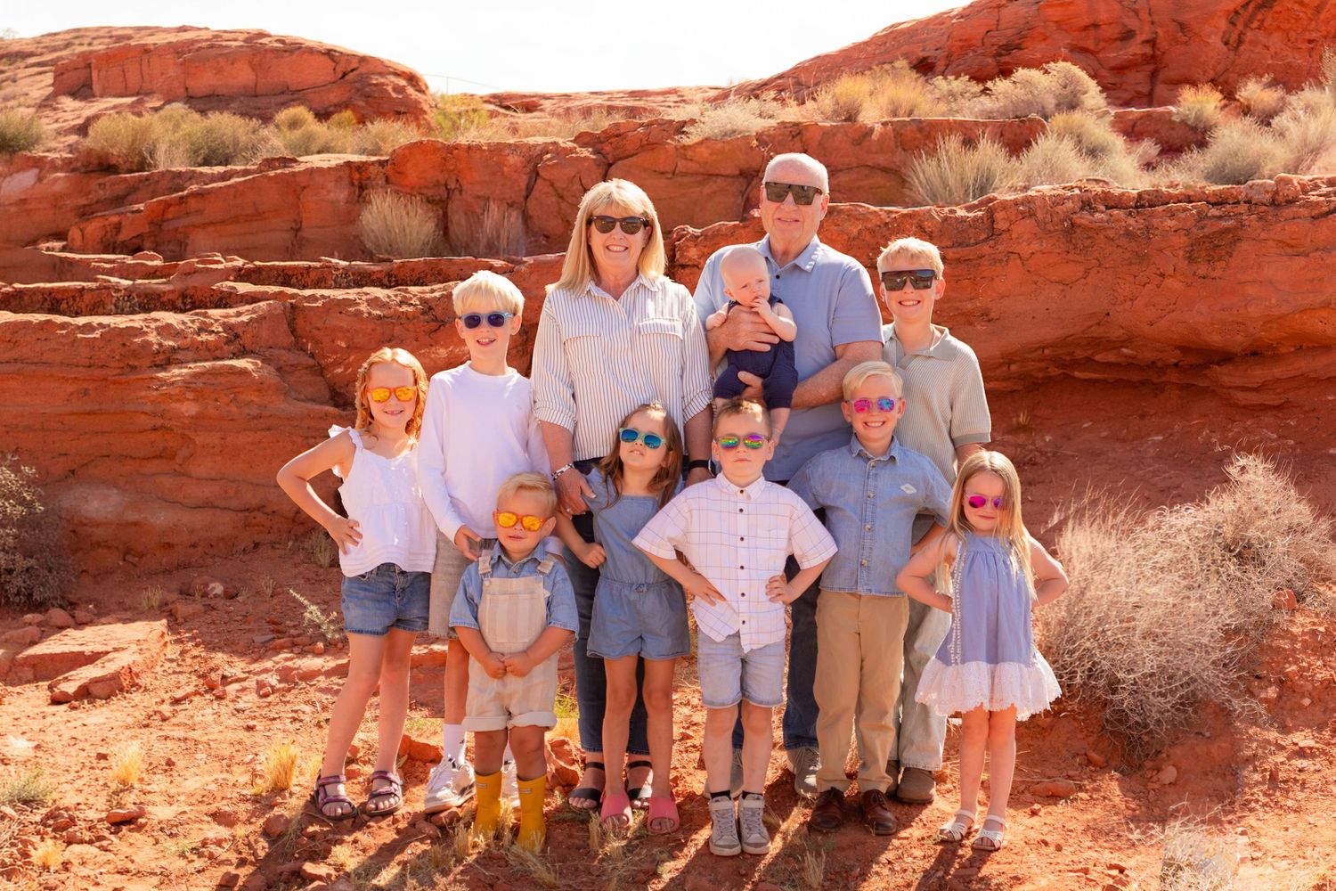 Large family group photo with children and adults posing among red rock formations in a desert landscape.