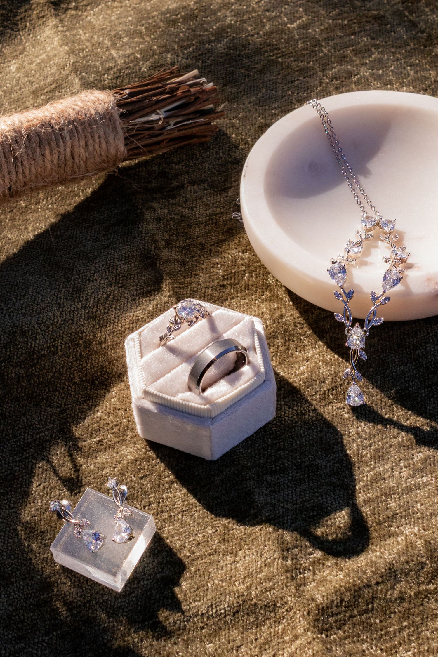Elegant silver jewelry set with gemstone necklace, ring in white box, and earrings on golden velvet fabric.