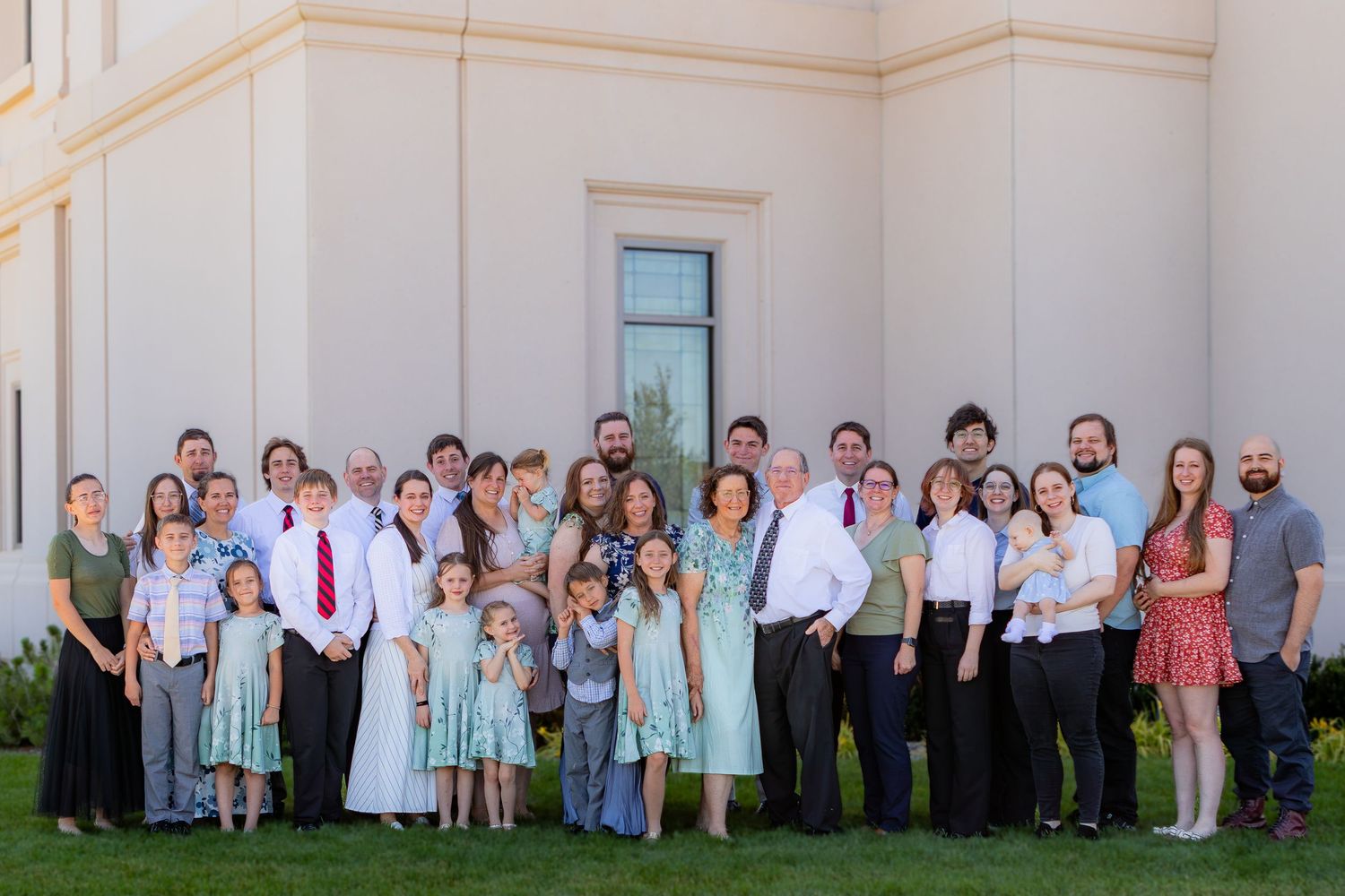Large family group portrait posing outdoors in front of a white building, dressed in formal attire.