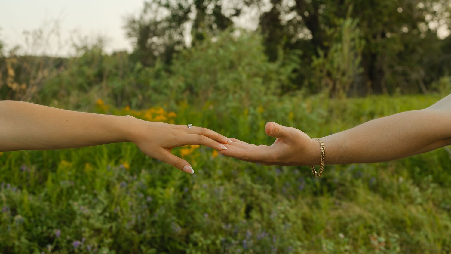 A close-up of a couple reaching for each other's hands over a grassy field during an engagement photography session in Calgary, Alberta.