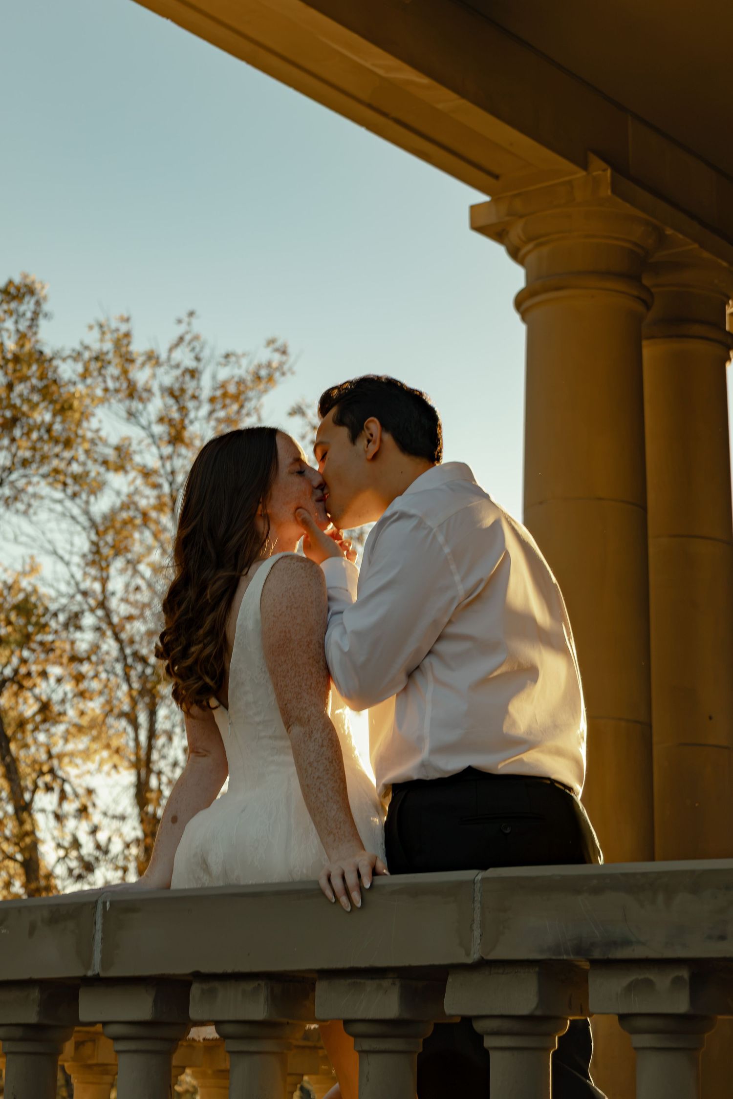 A newlywed couple sharing a kiss on a balcony in the warm evening light in Edmonton, Alberta.
