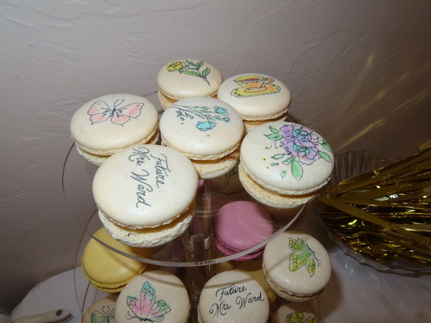 Decorated macarons on tiered stand with floral and butterfly designs for bridal shower.