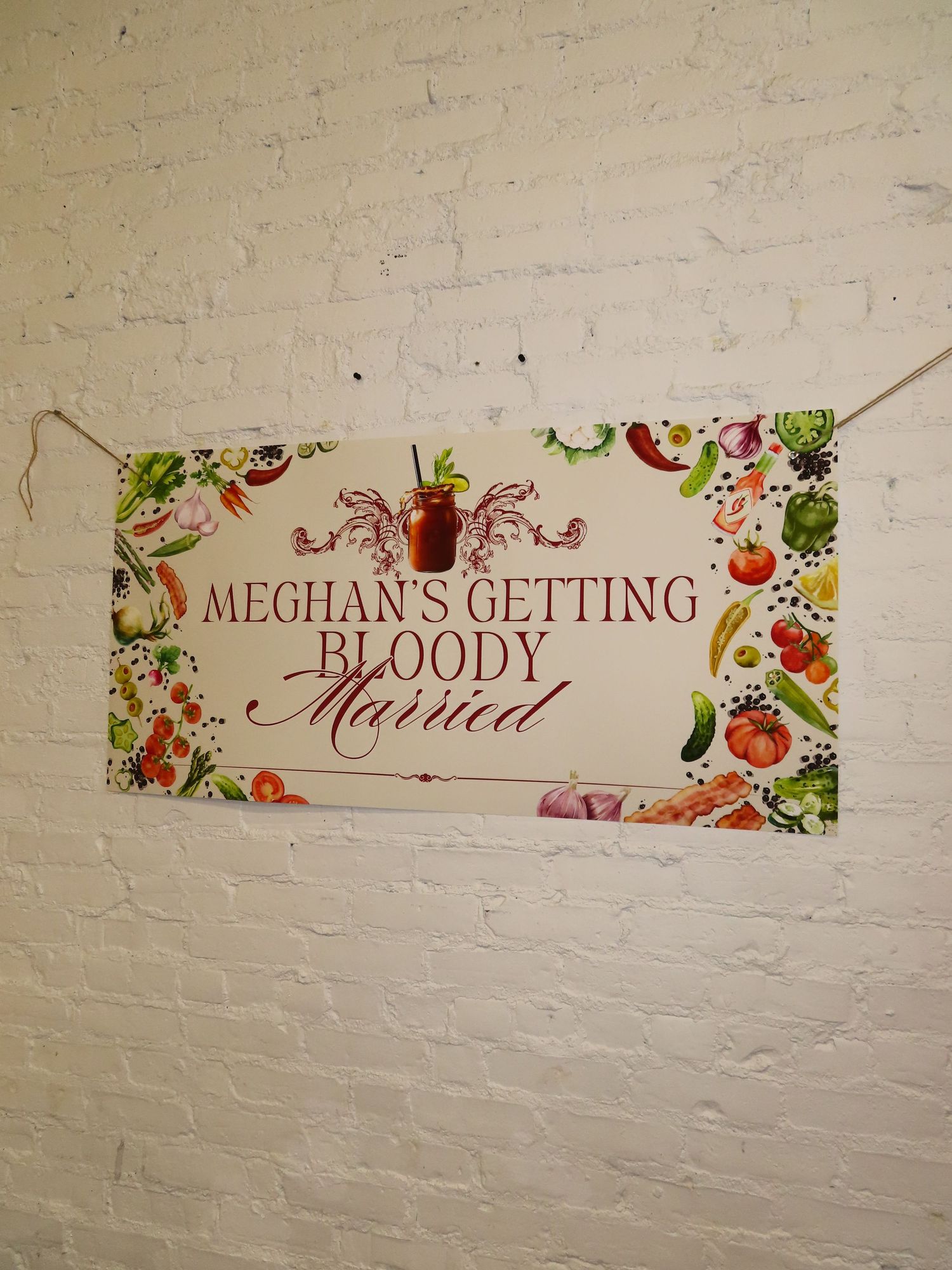 Banner on white brick wall reading Meghans Getting Bloody Married with vegetable decorations.