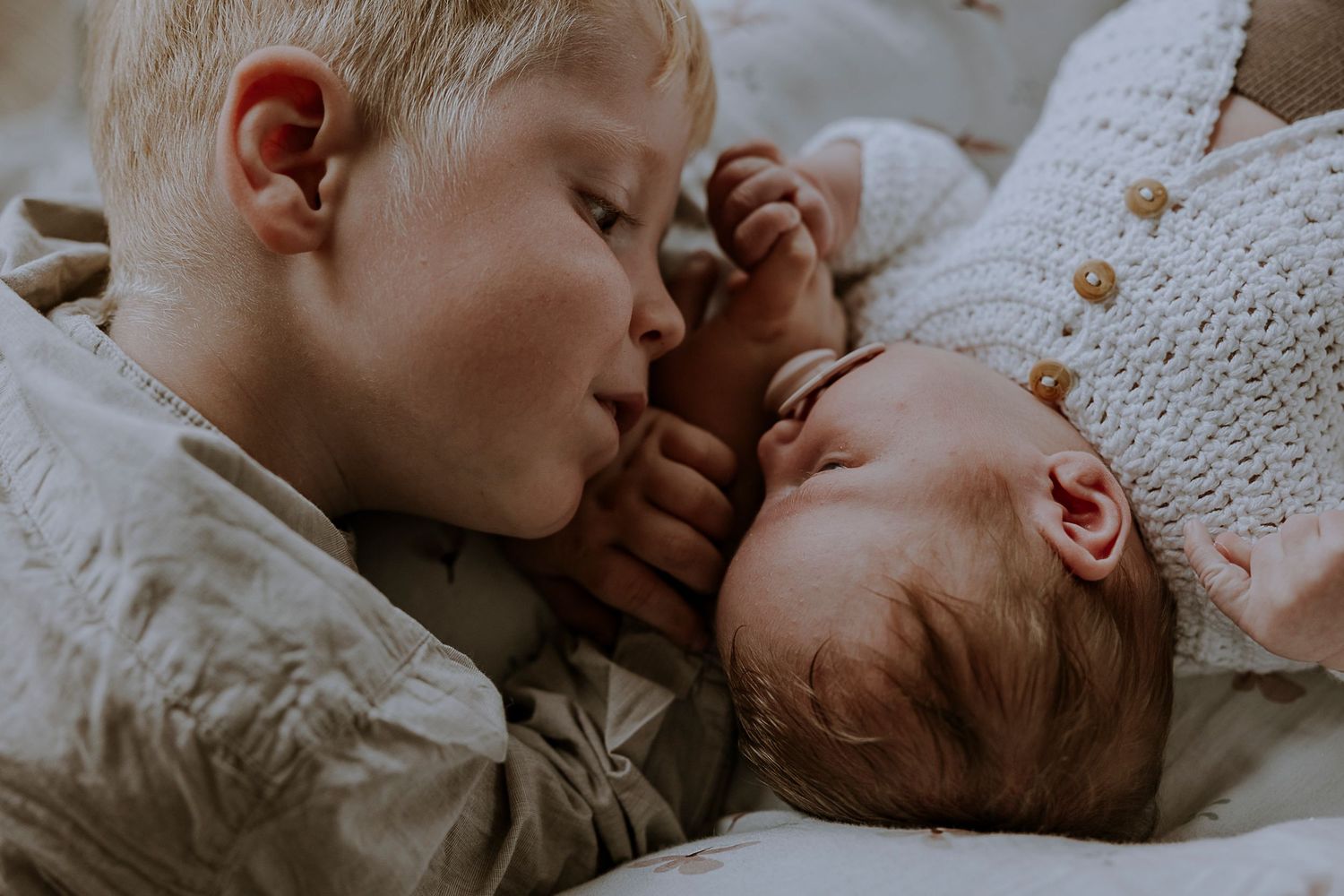 Intimate moment between siblings as they rest together on white bedding.