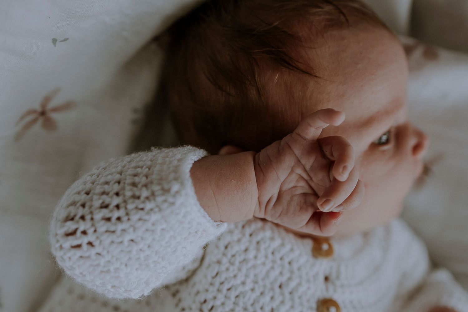 Baby's delicate hand resting on white knitted fabric.
