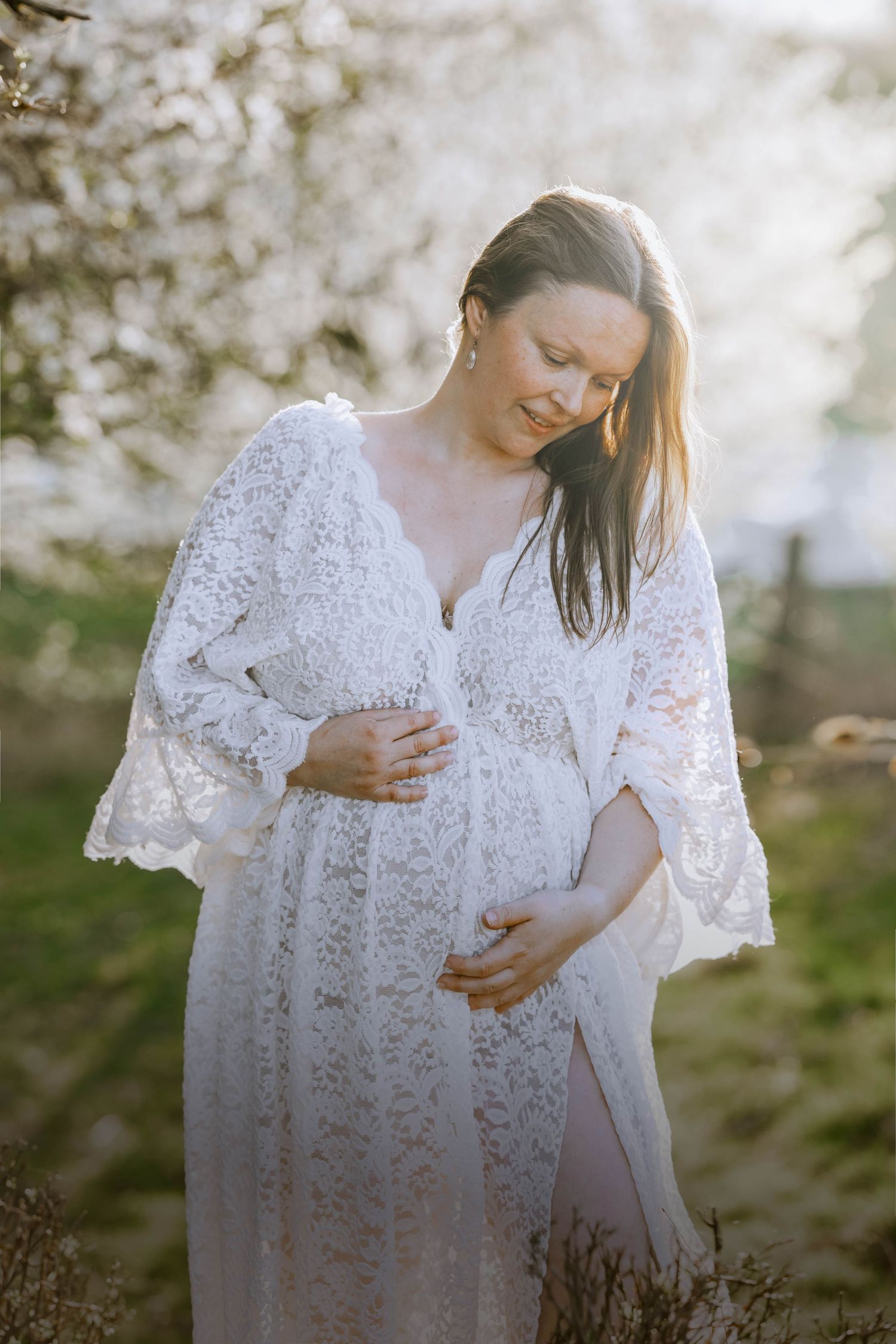 Ethereal maternity photo featuring a flowing white lace dress with bell sleeves in soft natural lighting.
