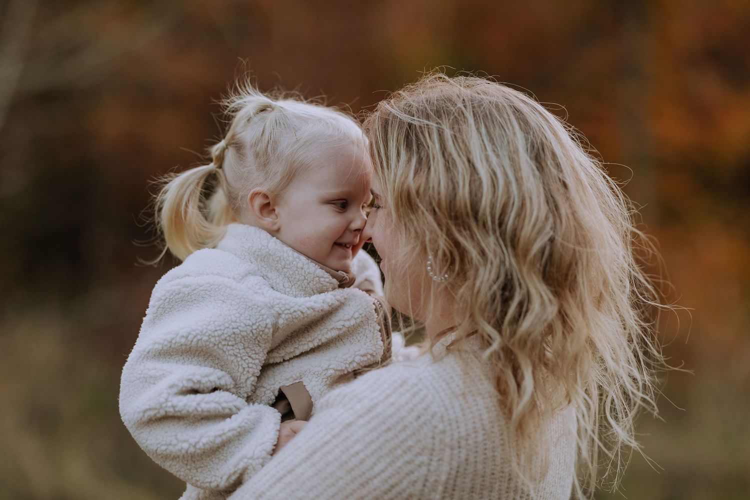 A parent and child share a tender moment outdoors during autumn with warm golden light filtering through trees.