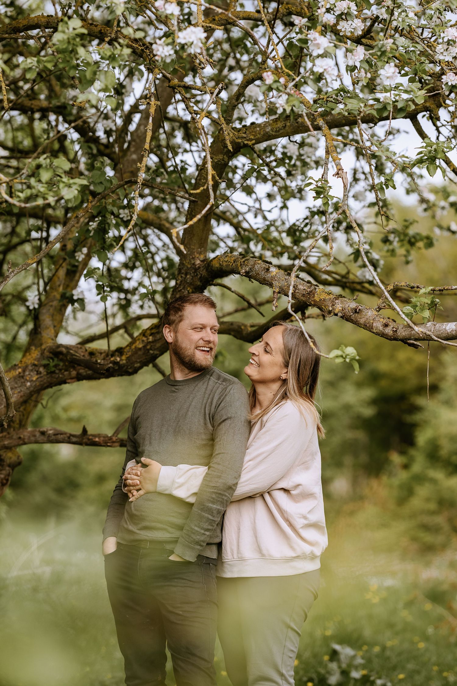 Happy couple embracing and laughing under blooming spring tree in garden setting.