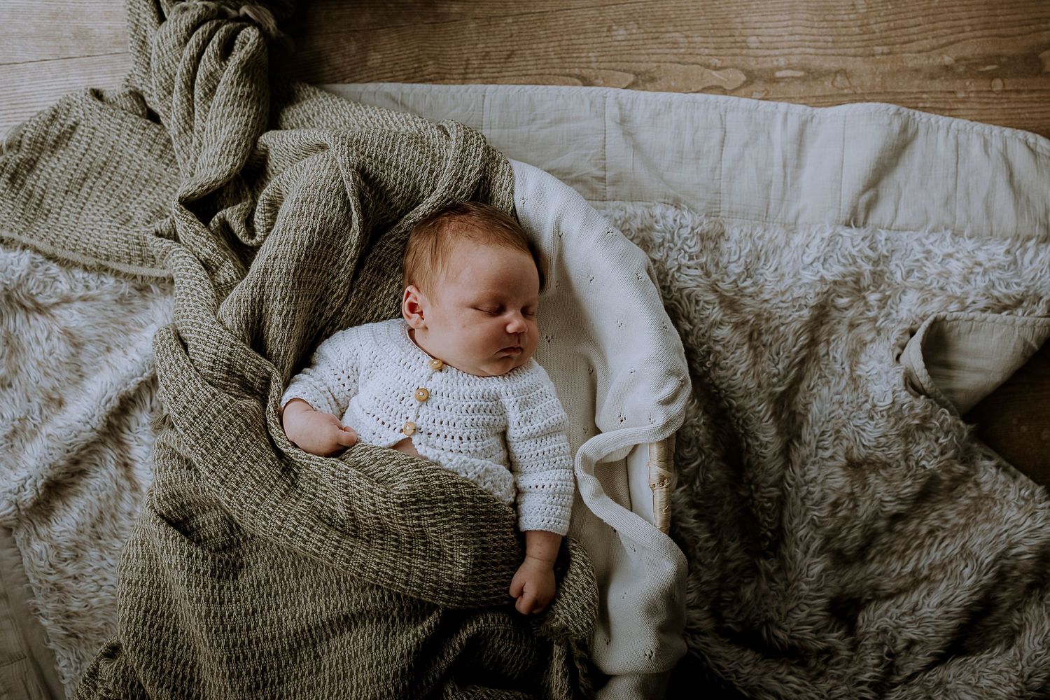 A baby dressed in white sleeps peacefully on cozy knitted blankets.