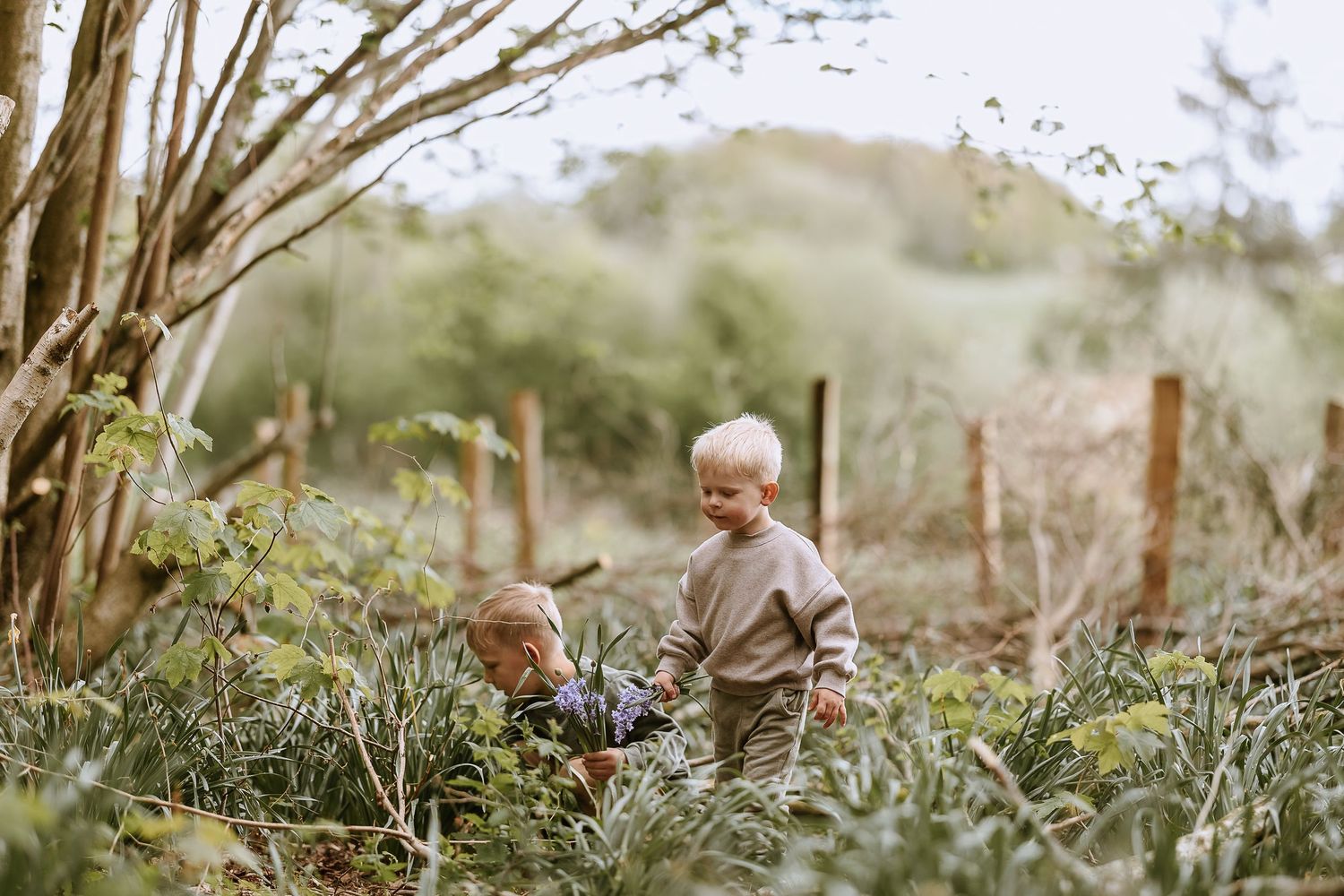 Children exploring among plants and wooden posts in outdoor garden.