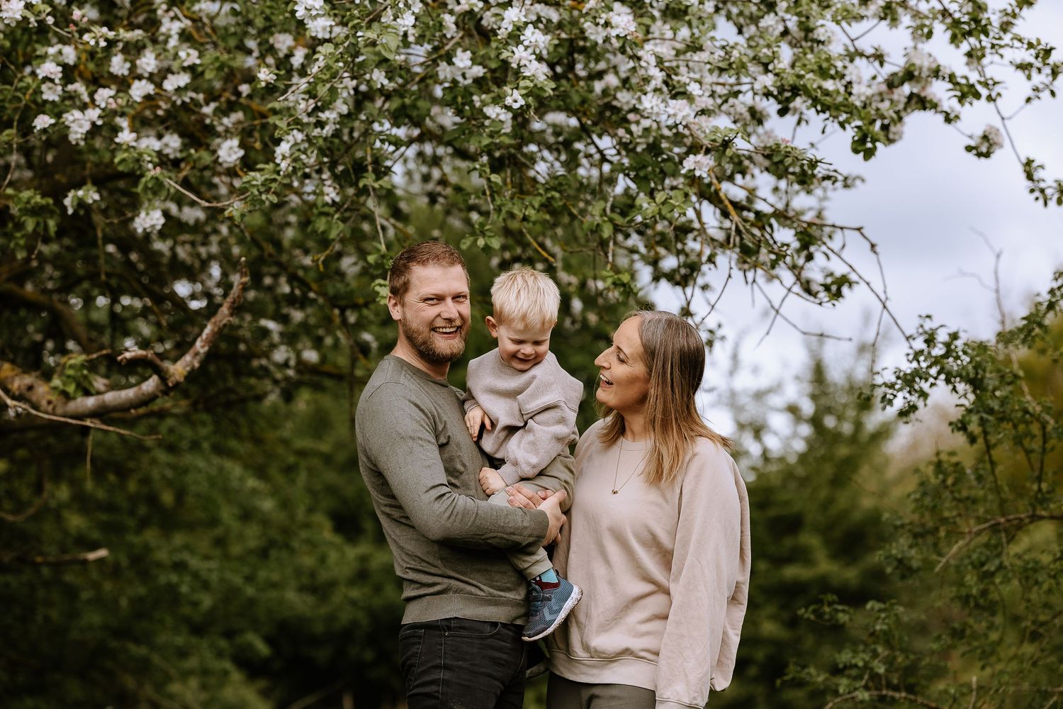 Family of three enjoying a spring day together under flowering tree branches.