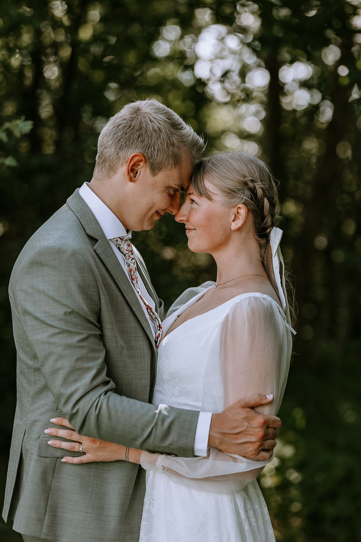A tender moment between newlyweds as they embrace outdoors, with the bride in white and groom in gray.