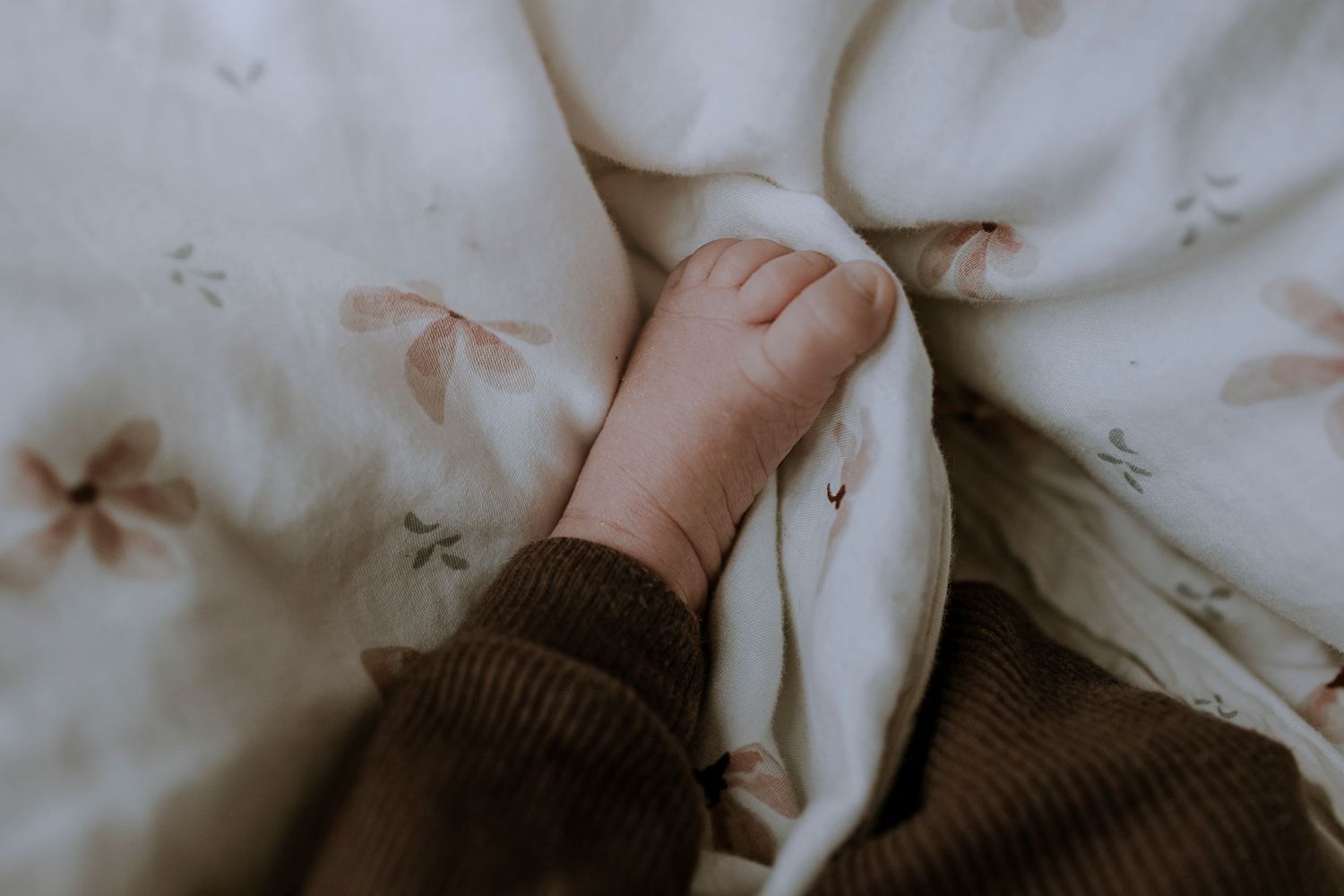 Small hand grasps white bedding with delicate star patterns in a soft, muted setting.
