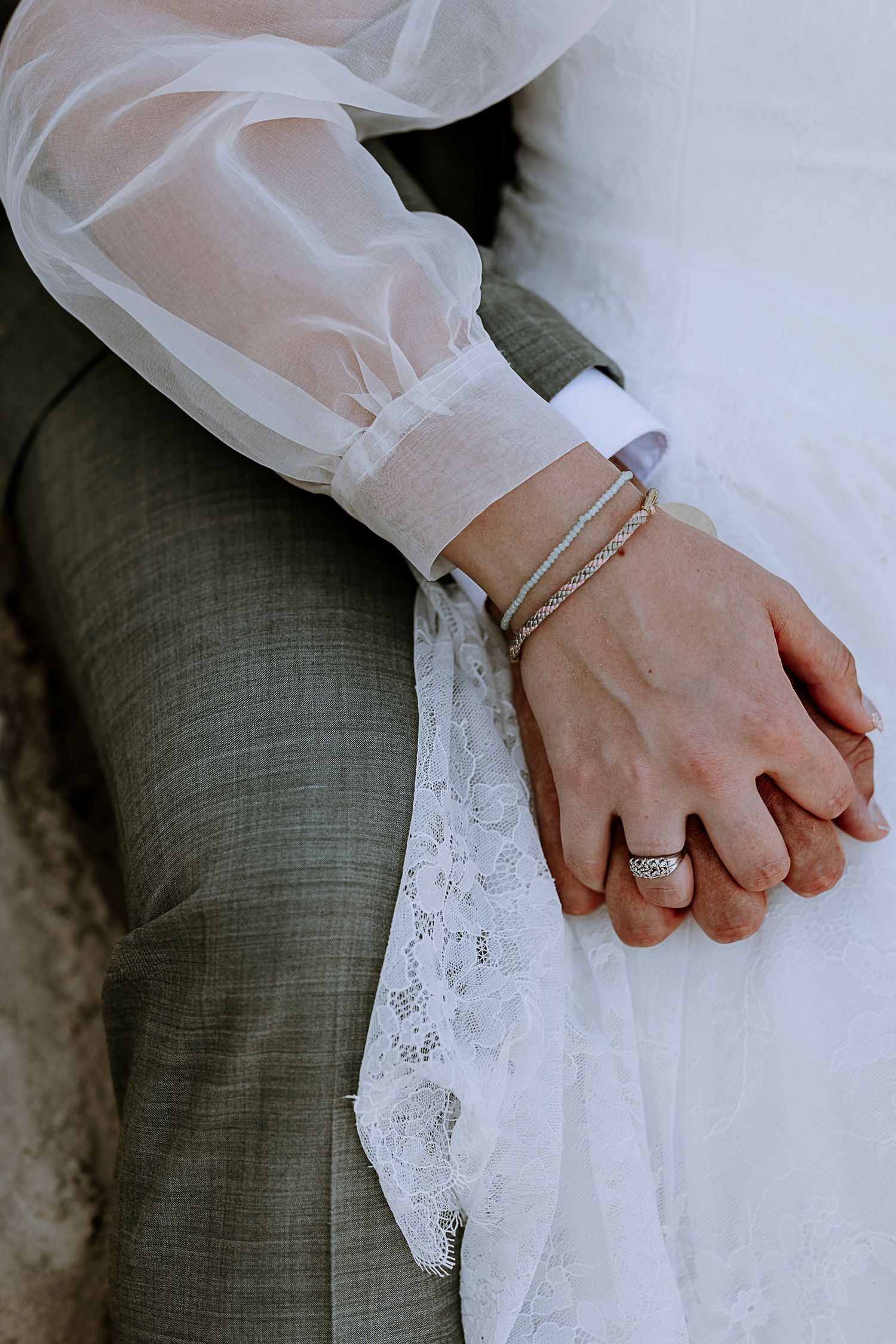 Close-up of newlyweds holding hands, showing wedding rings and bridal gown details.