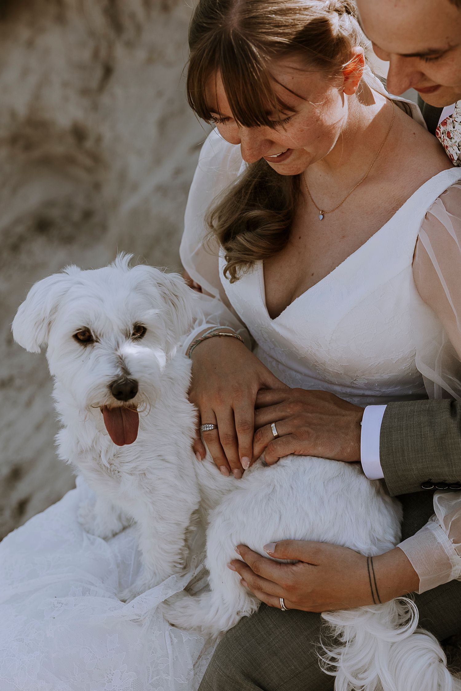 A happy white dog sits with the newlyweds, showing off their wedding rings.