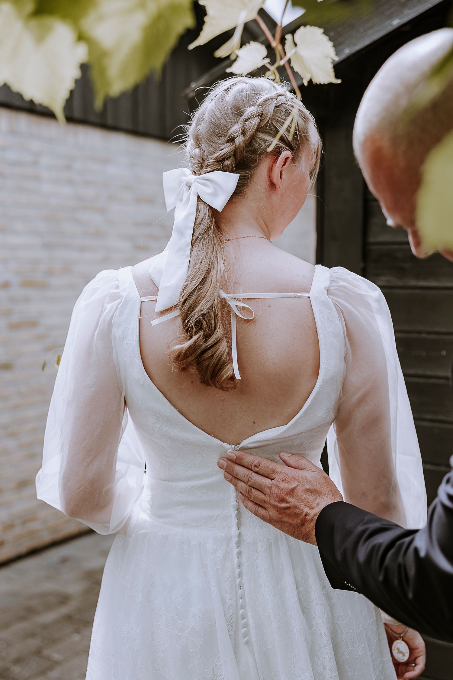 Back view of vintage-inspired wedding dress with sheer sleeves and button details.