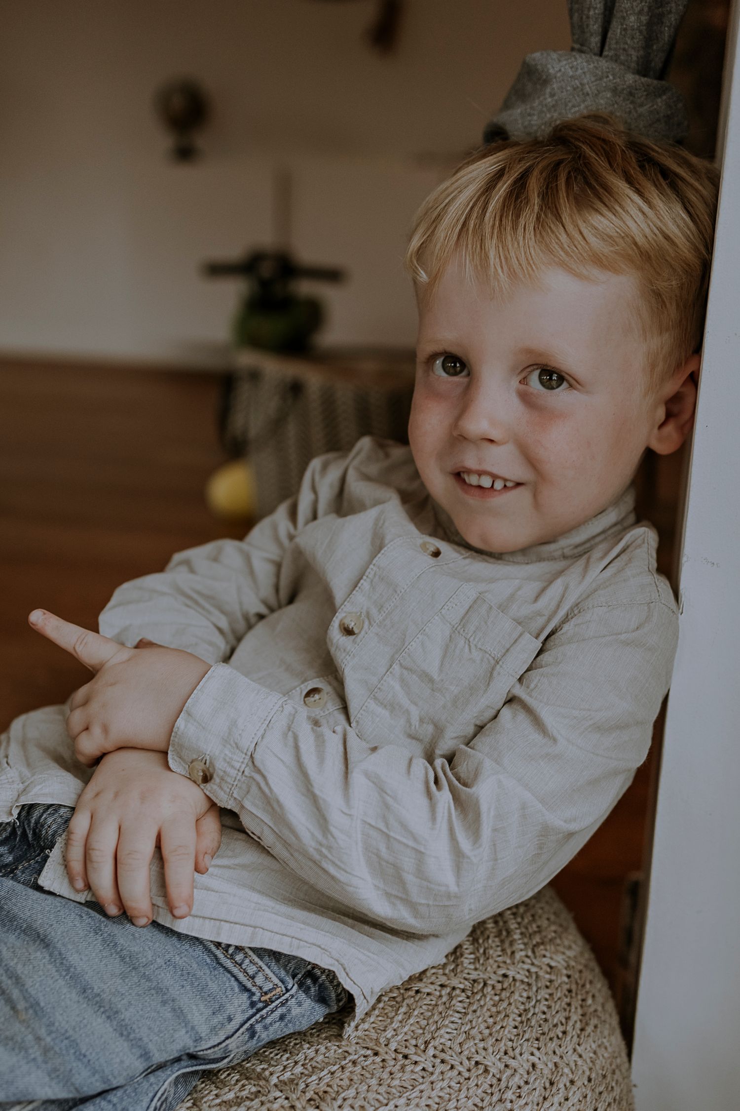 Child relaxing on a woven pouf chair with a cheerful expression.
