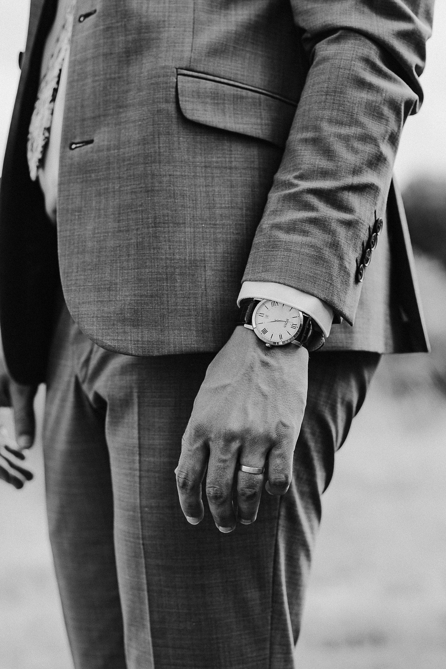 Black and white detail shot of grey suit sleeve with watch and wedding ring.