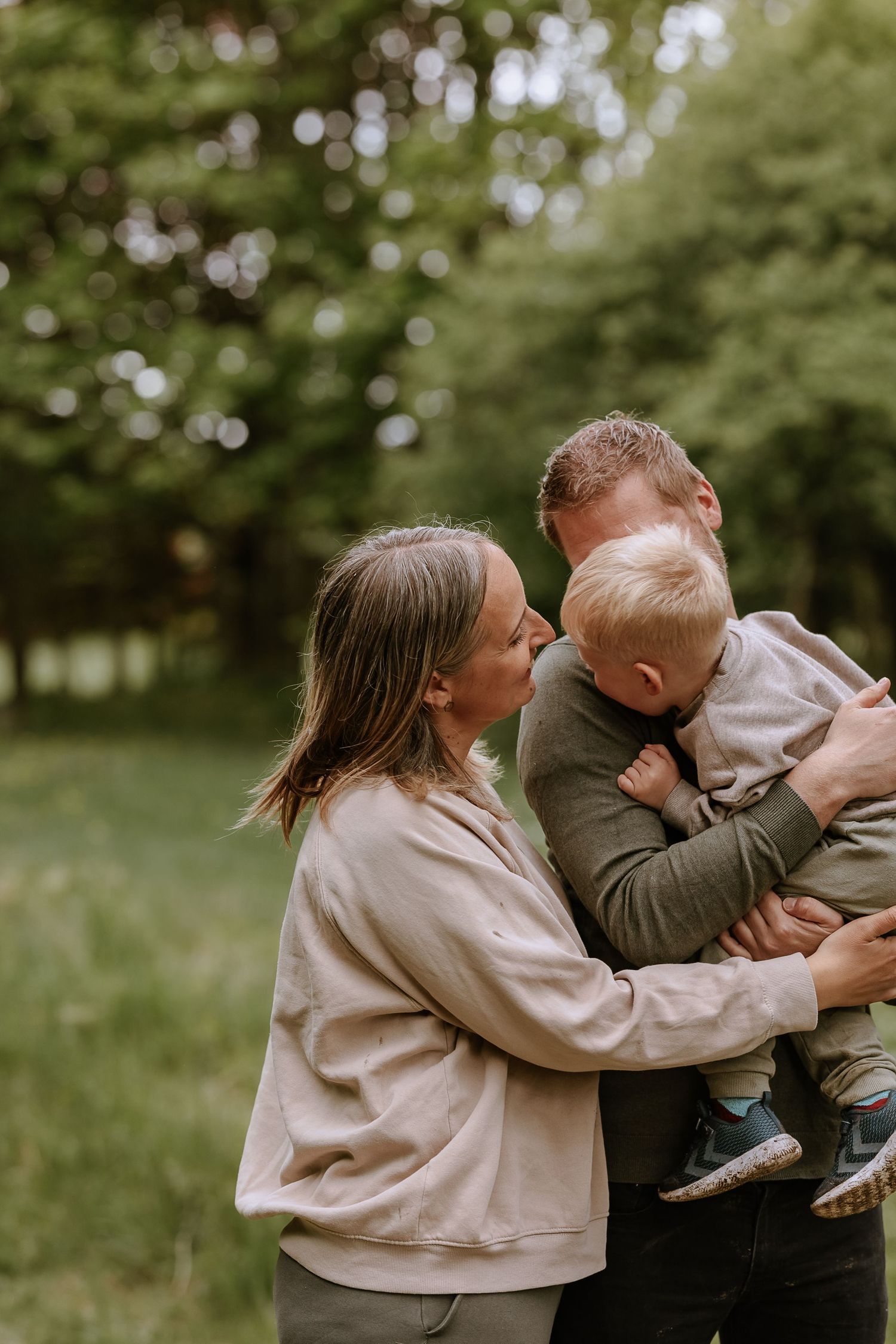 Family shares joyful embrace in nature setting with green bokeh background.