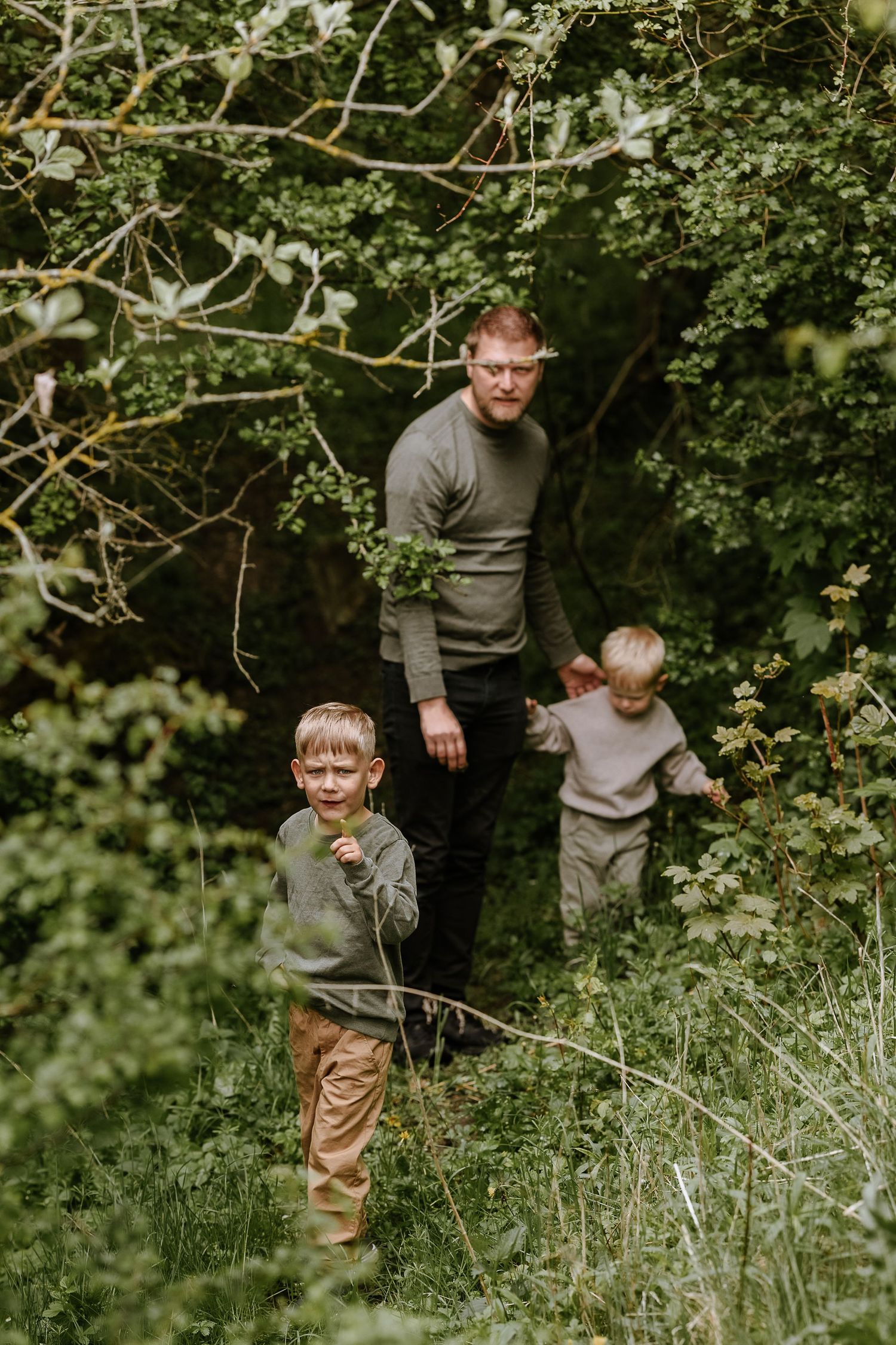 Three people explore a wooded area together wearing coordinating gray sweaters.