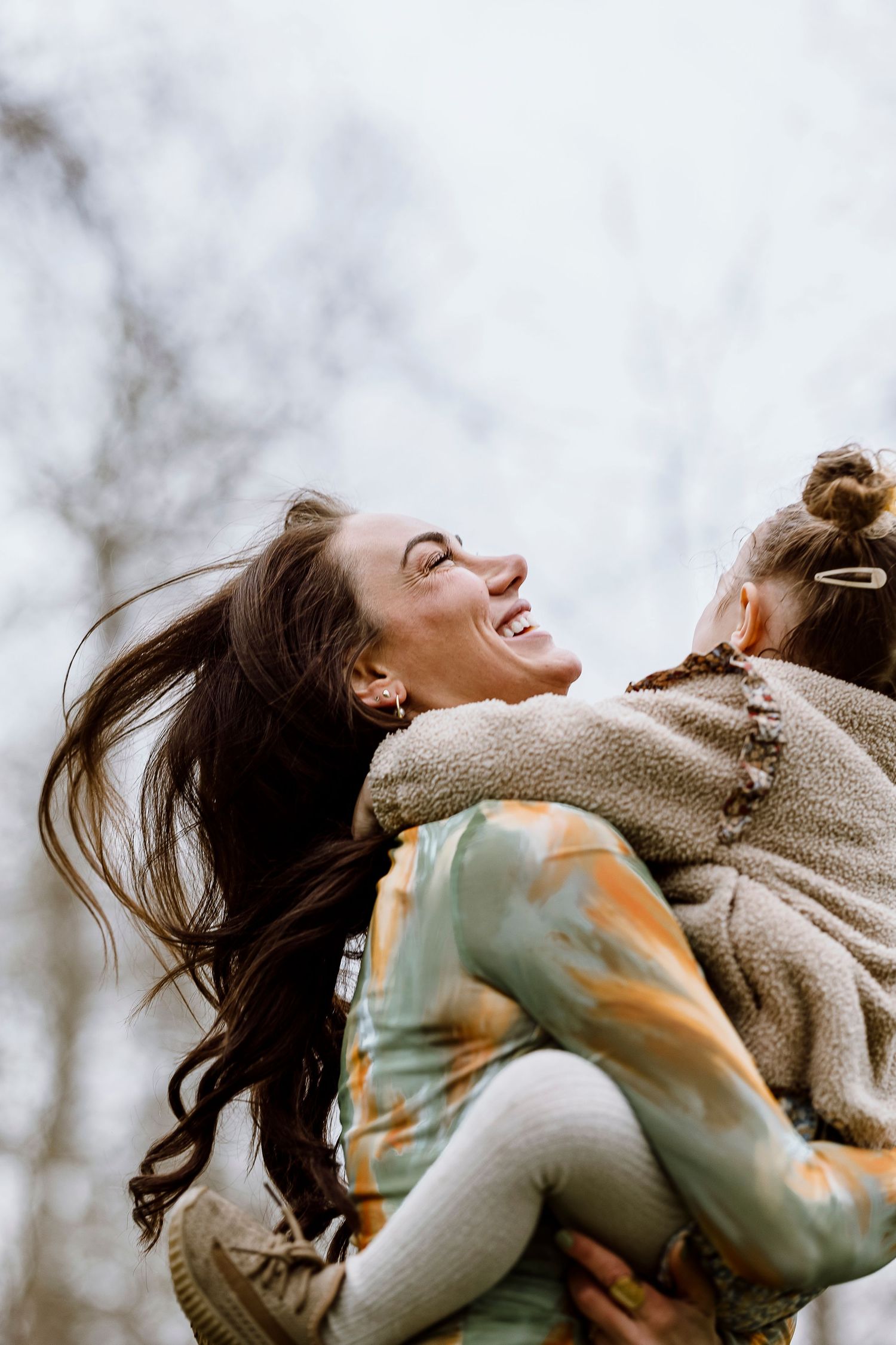 Two people embrace joyfully while wearing cozy sweaters outdoors on a cloudy winter day.
