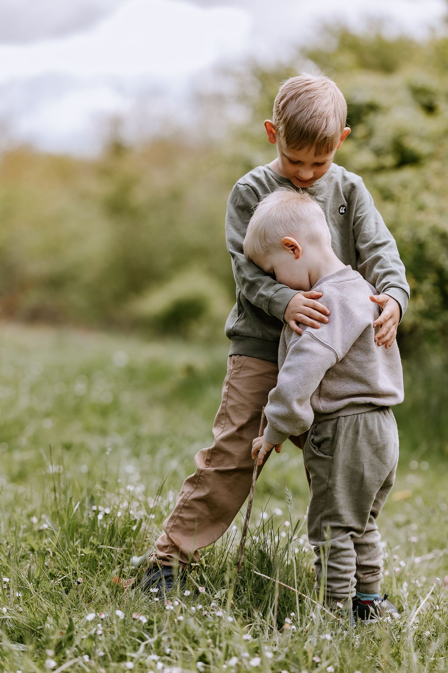 Two children in matching gray outfits playing together in a grassy meadow.