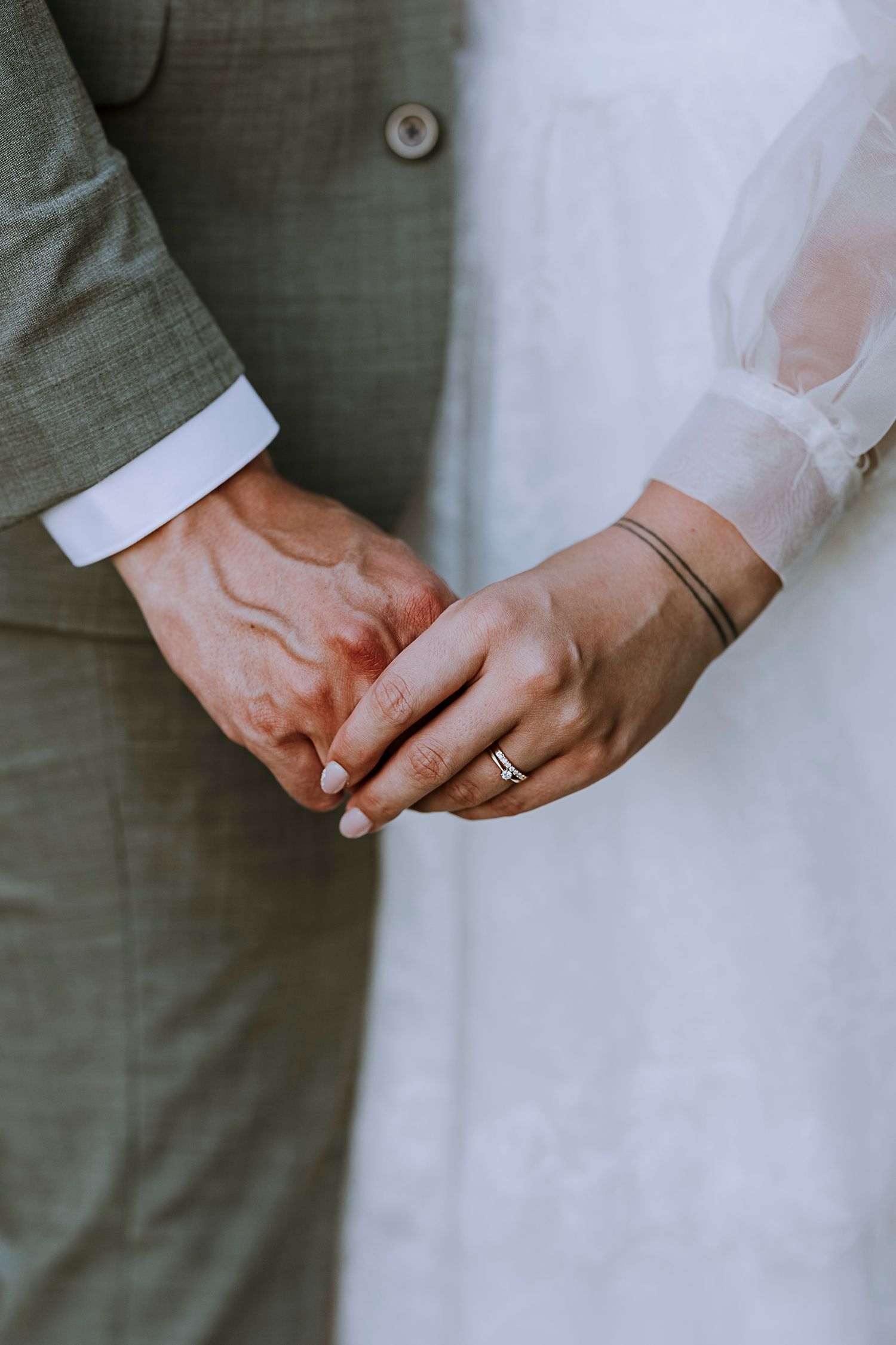 Close-up of newlyweds' hands touching, showing wedding ring and dress details.