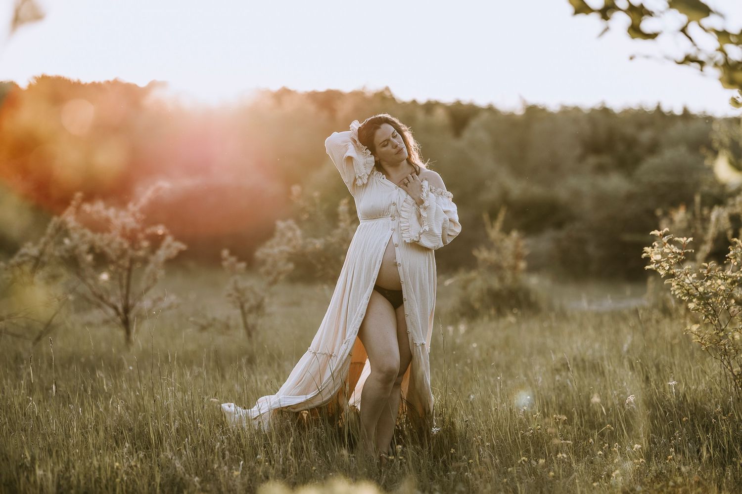 A romantic couple in white outfits embraces in a sun-drenched meadow at golden hour.