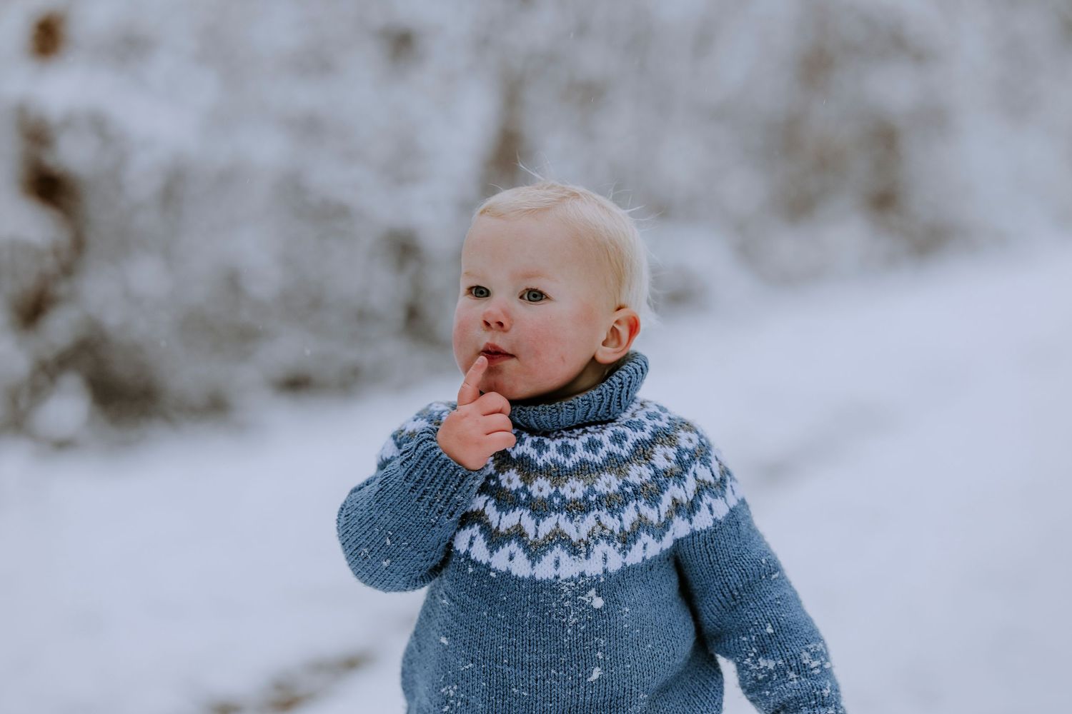 Small child wearing blue Nordic patterned sweater in snowy winter setting.