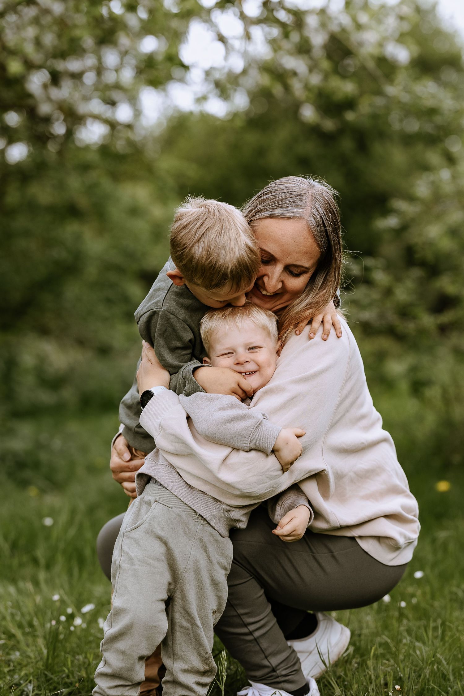 Loving parent embracing two children in casual outdoor spring setting.