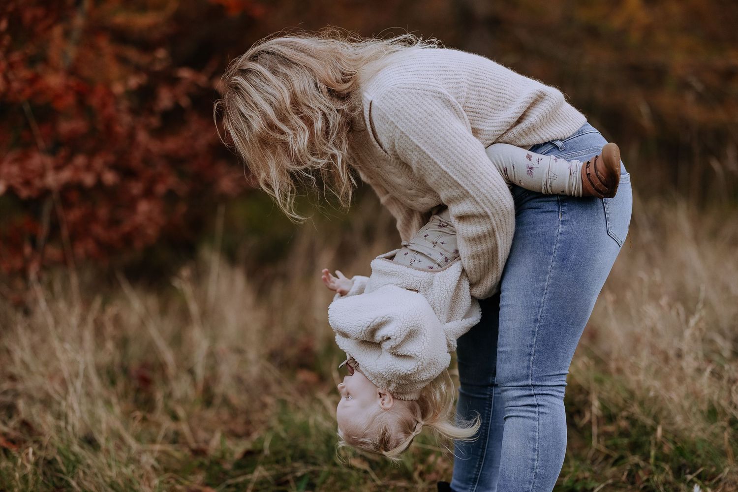 Playful interaction between parent and baby against a backdrop of autumn colors and tall grass.