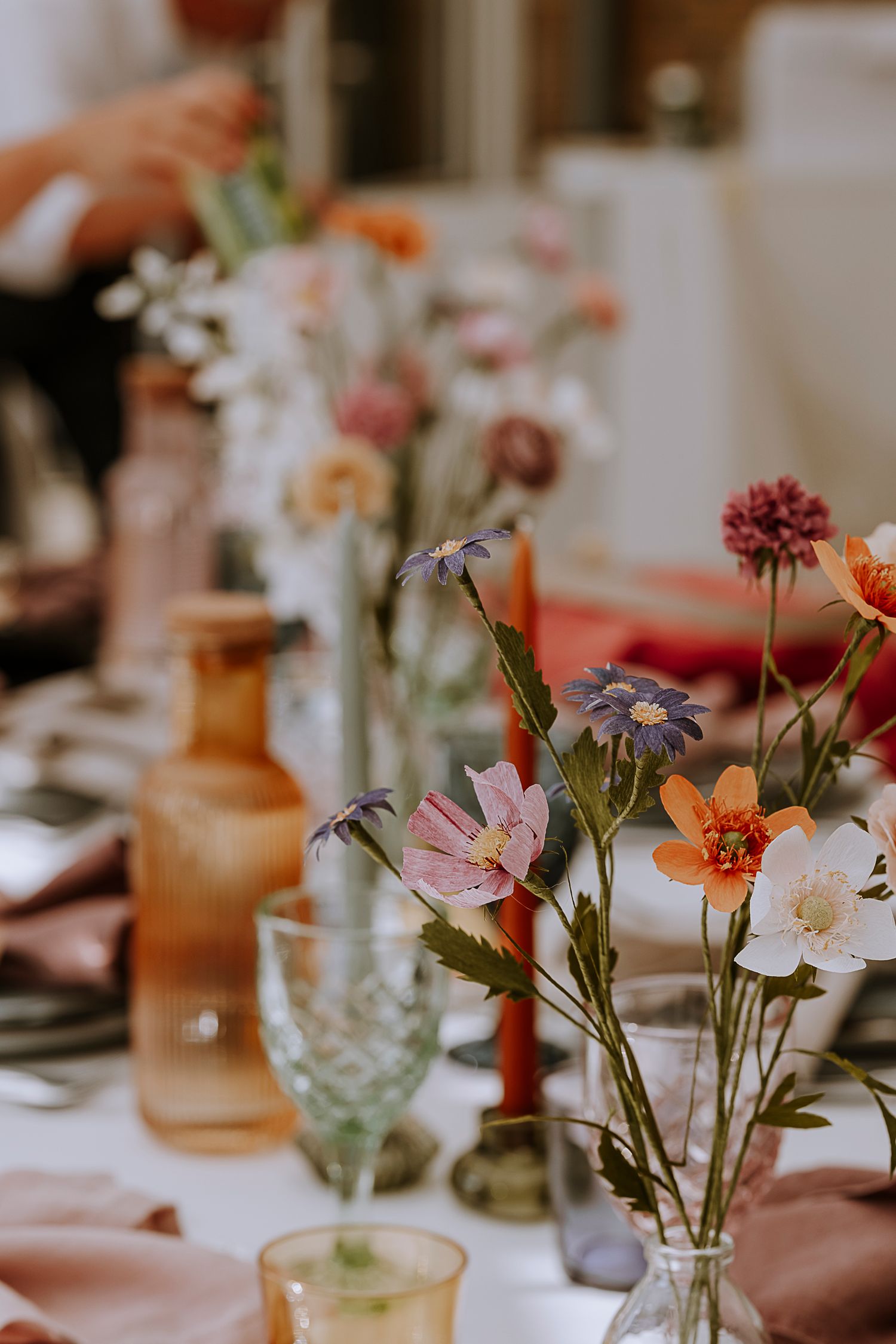 Close-up of colorful wildflower arrangements in glass vases on white tablecloth.