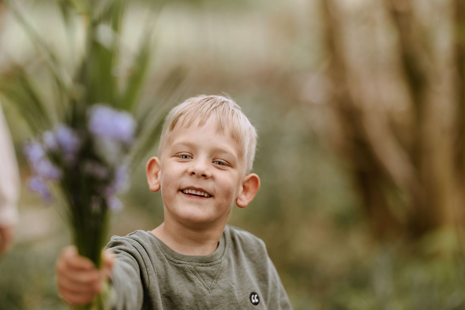 Child in gray shirt holding purple flowers with joyful expression.