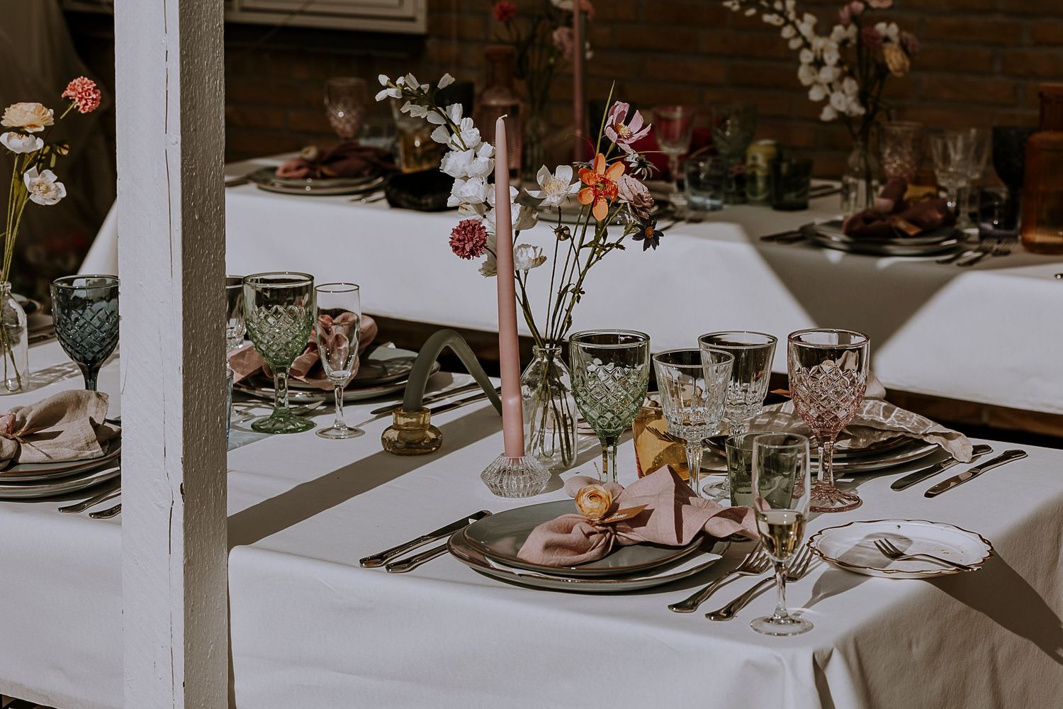 Wedding reception tables set with elegant place settings, flowers, and glassware under outdoor canopy.