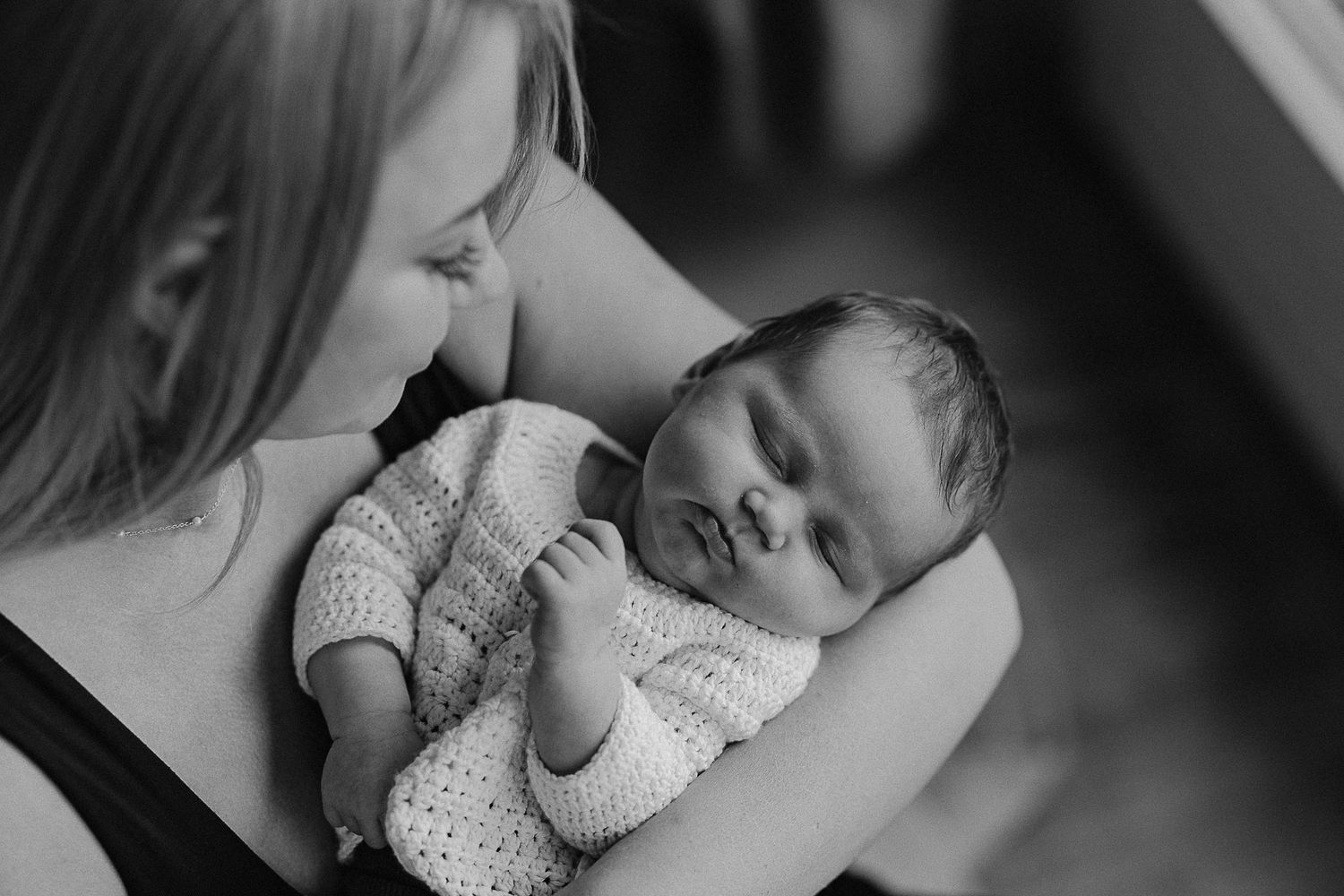 Black and white portrait of parent cradling sleeping infant in knit outfit.