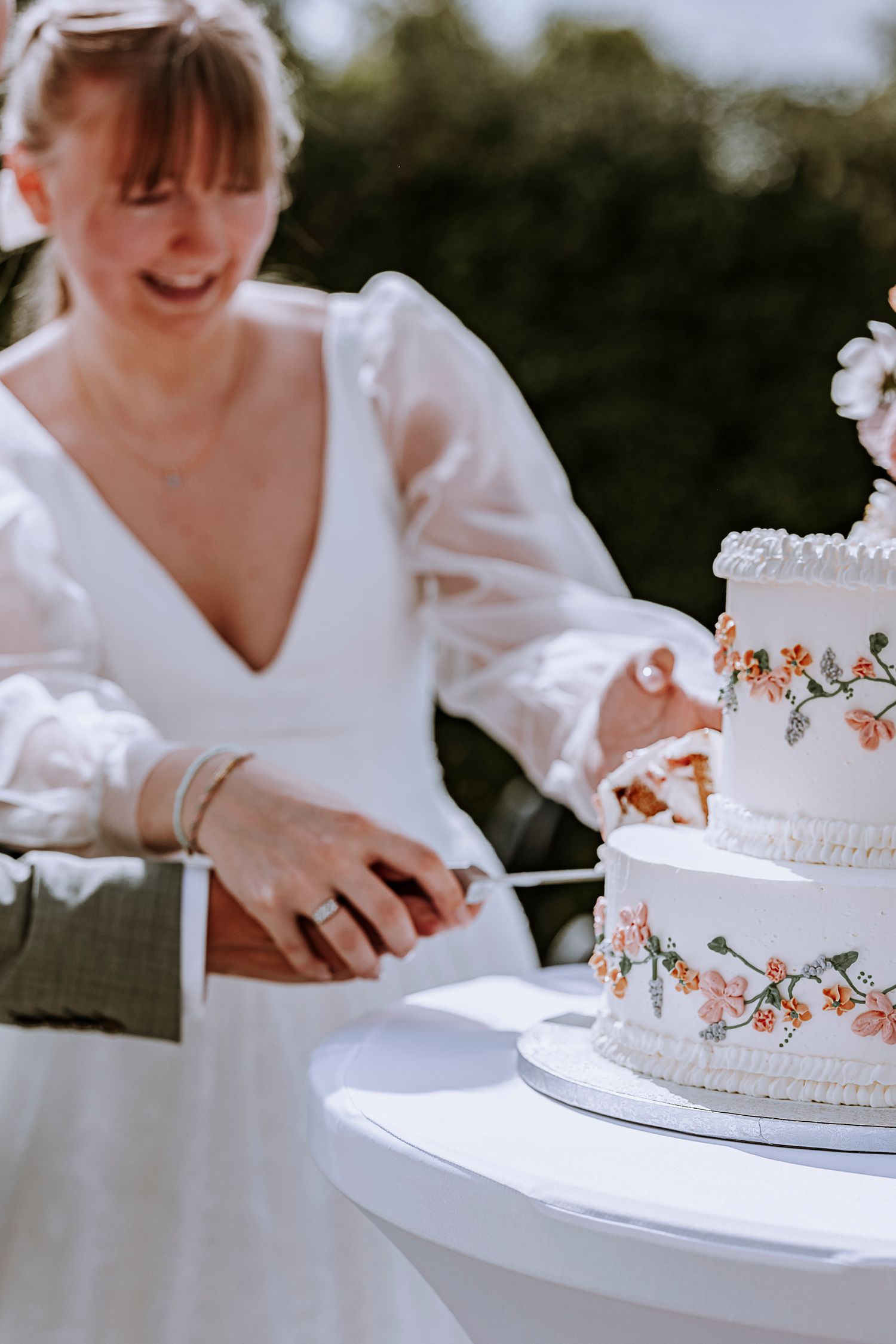 Wedding cake with delicate floral decorations being cut on white table.