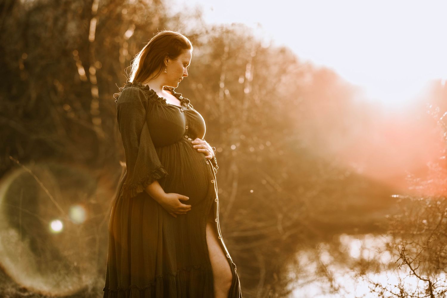 Golden hour maternity photo with sun flare and flowing dark dress.