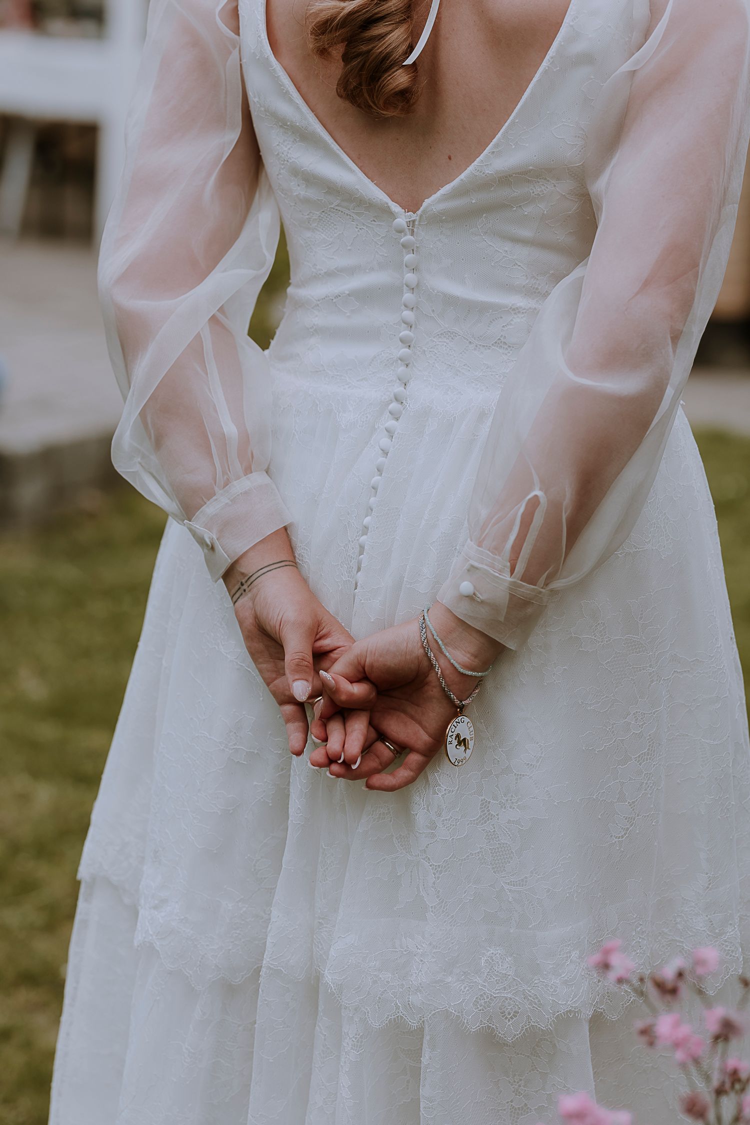 Close-up of wedding dress showing delicate sheer sleeves and clasped hands.