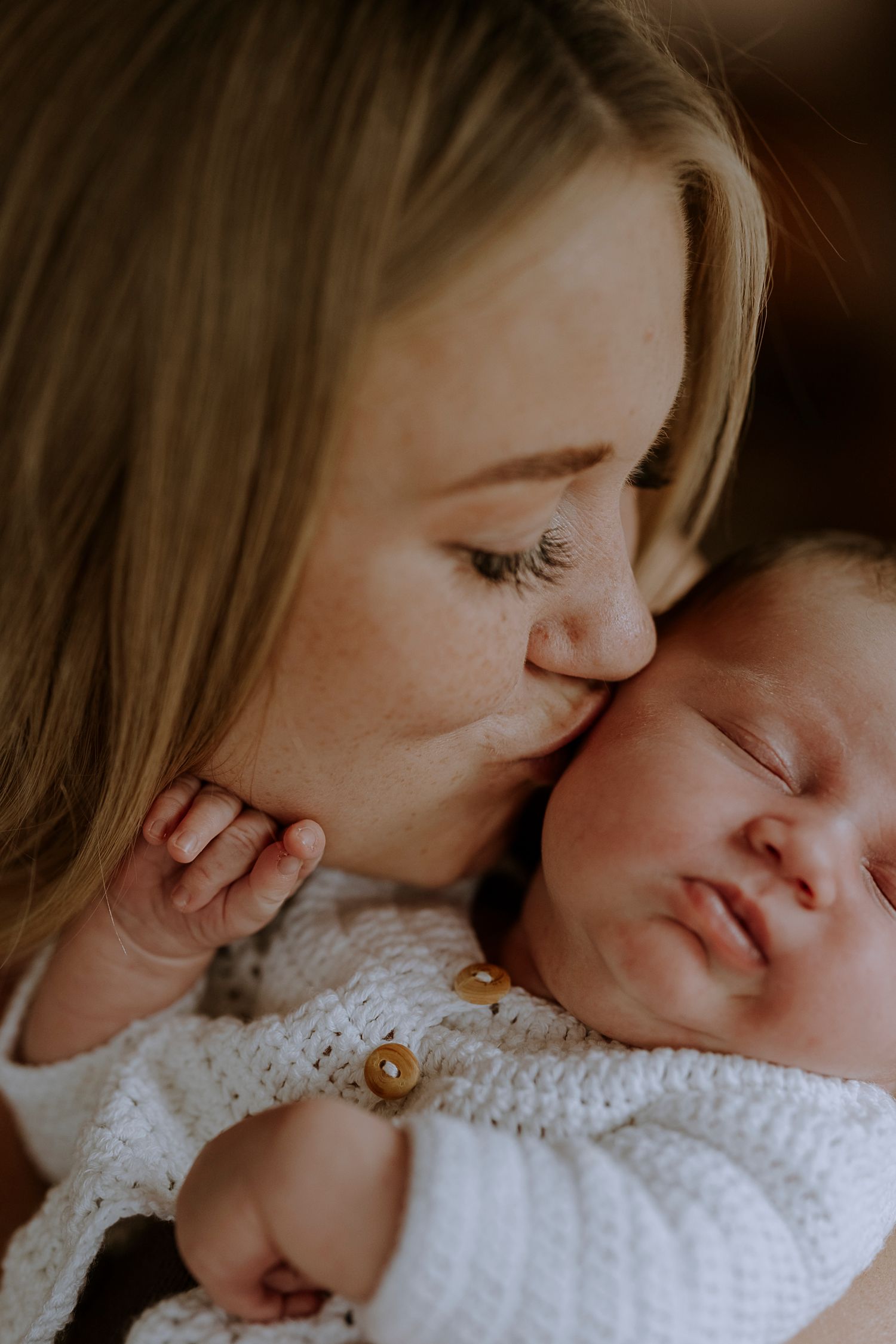 Tender moment of parent giving sleeping newborn in white knit sweater a gentle kiss.