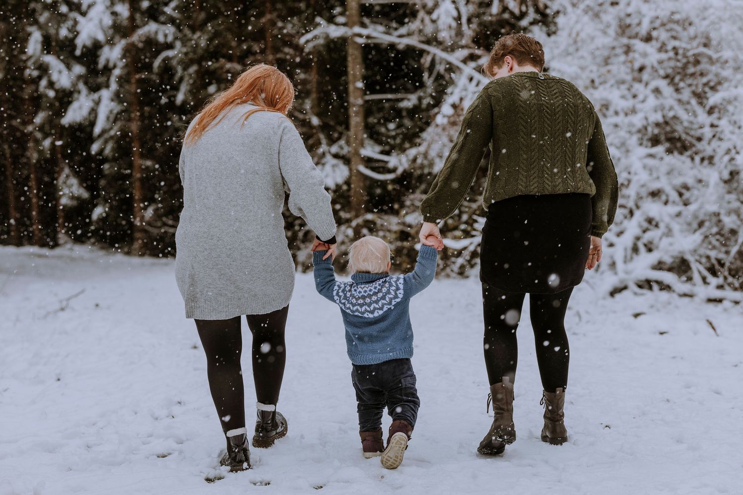 Family walking hand in hand through snowy forest path in winter.