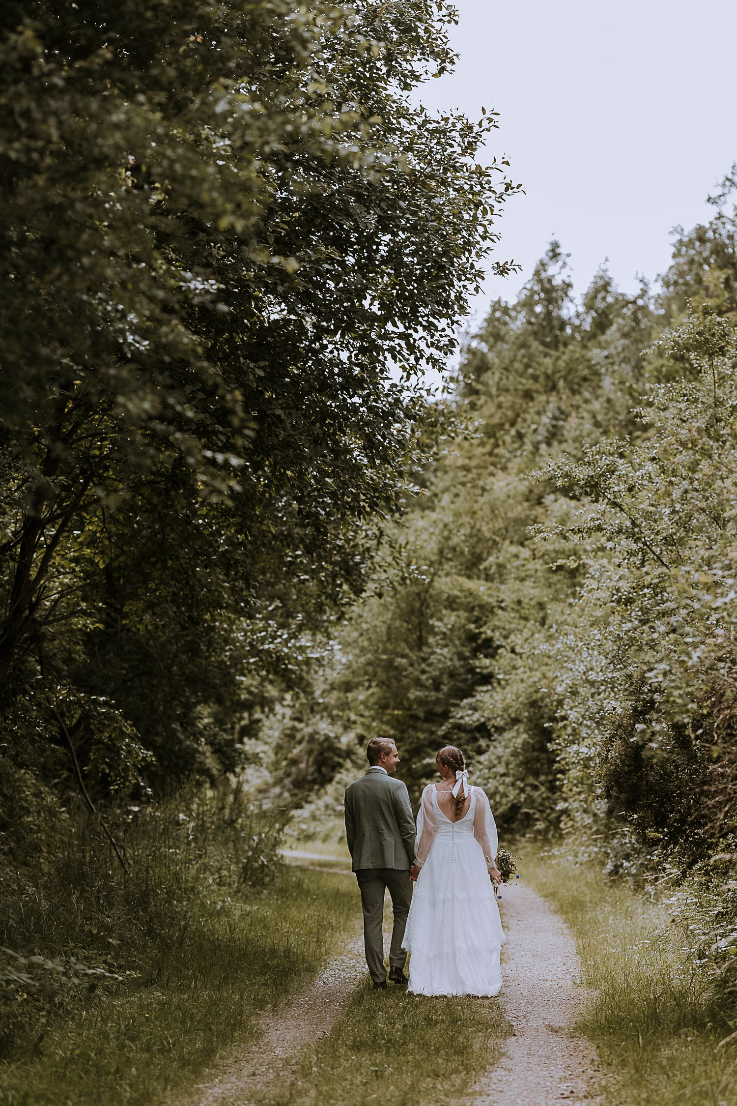 Couple walking down wooded path in wedding attire.