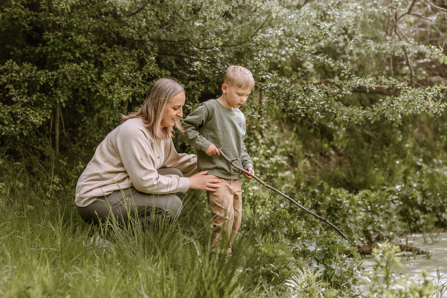 Two people sitting together in a lush green meadow surrounded by blooming spring foliage.