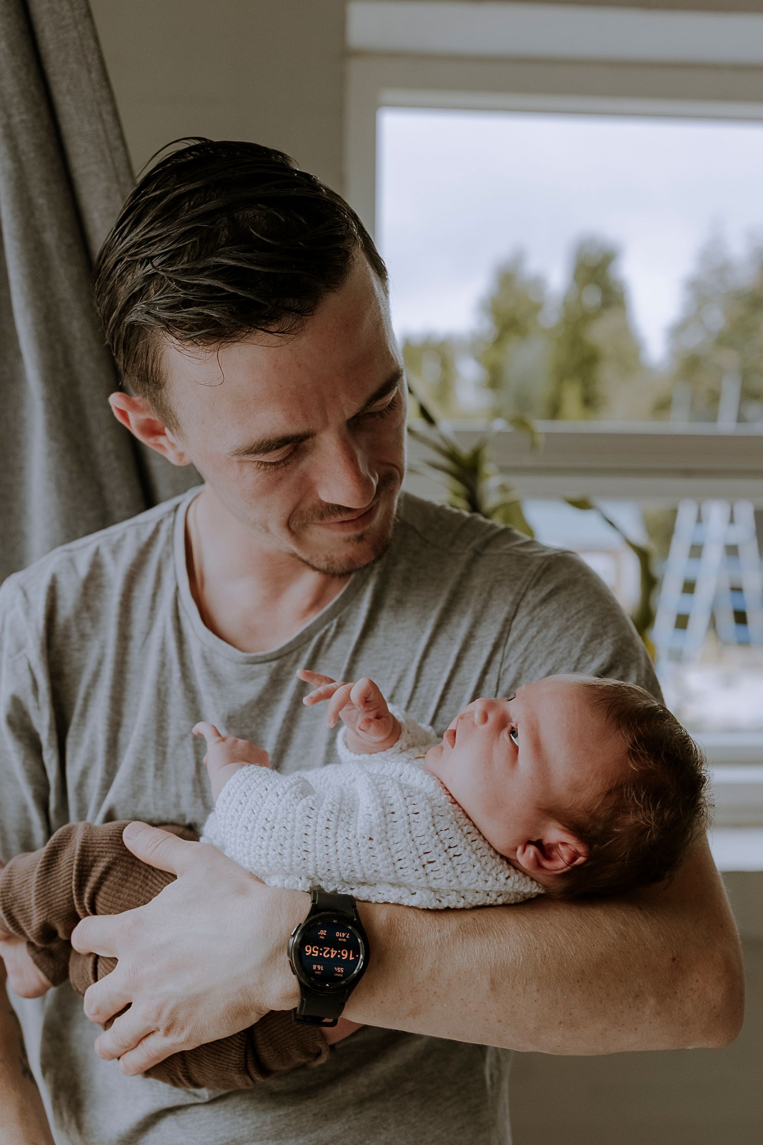 Parent in grey t-shirt tenderly holds newborn baby in white knit sweater.