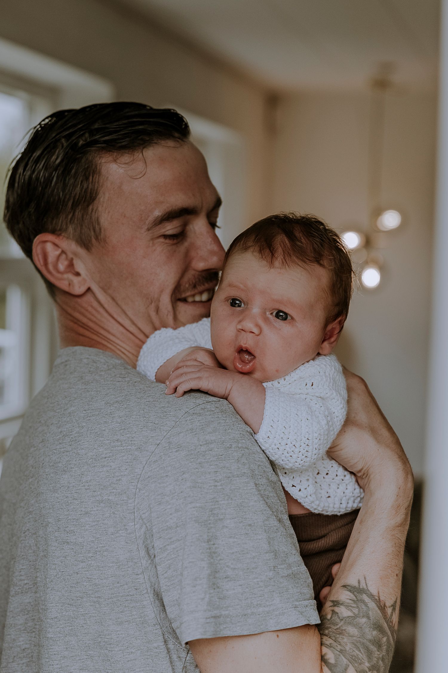 Parent in grey t-shirt holds baby wearing white knit sweater against shoulder.