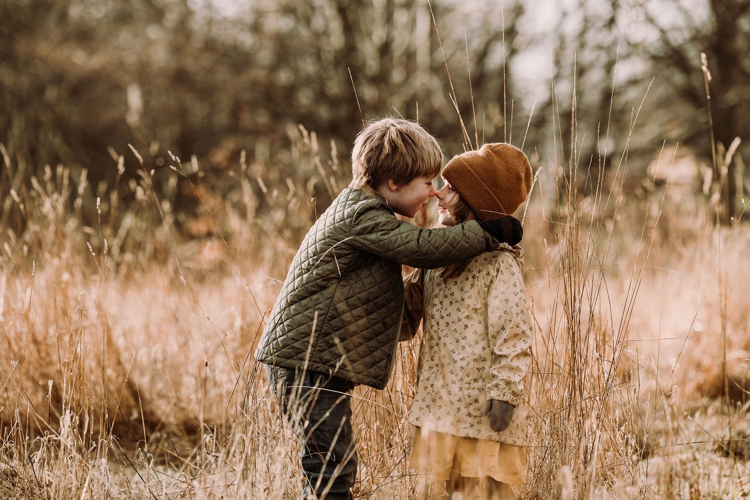 A couple in warm autumn clothing walks through a golden field during sunset holding hands and embracing.